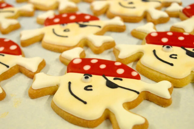 Cookies shaped like smiling pirates with red bandanas, decorated with white dots, black eyes, and smiling mouths.