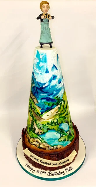 A hand painted sculptured cake with scenes from The Sound of Music with a model of Maria on the top for Matthew Bourne's 60th Birthday