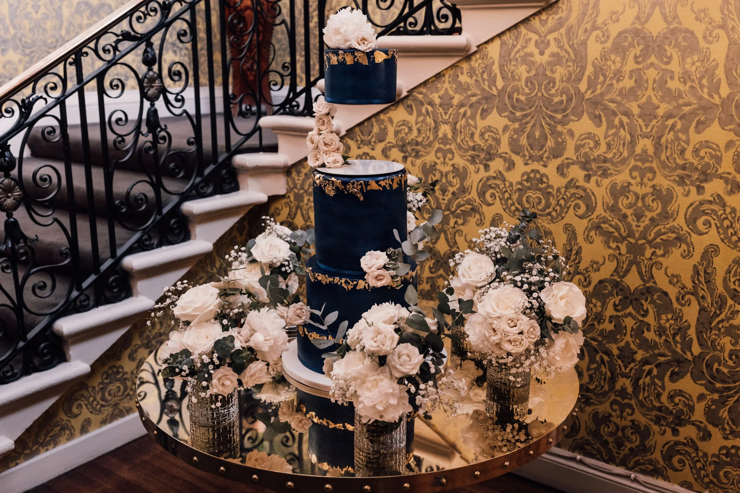 A luxury 3 tier wedding cake in navy blue with gold accents and a floating top tier