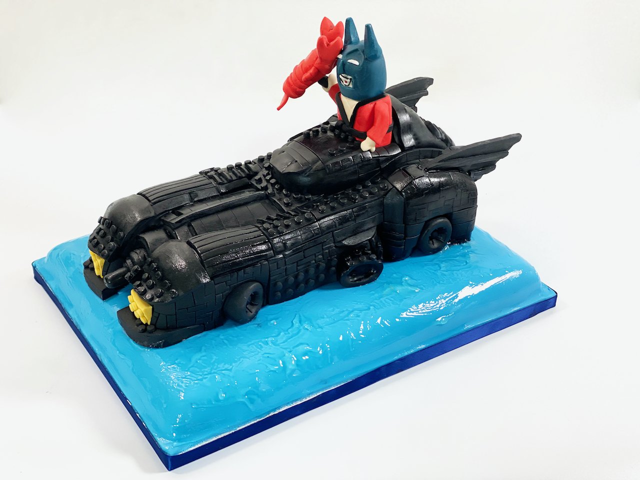 Lego batmobile with lego batman holding a lobster