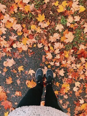 Black nikes against dark asphalt covered in gorgeous fall leaves. Grace wears black leggings and you can see a fuzzy grey pullover peeking out at the bottom of the photo