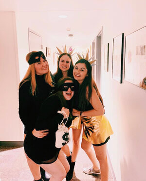 Four girls stand together smiling and hugging each other. They are dressed up for Halloween in DIY costumes as bank robbers and the sun.