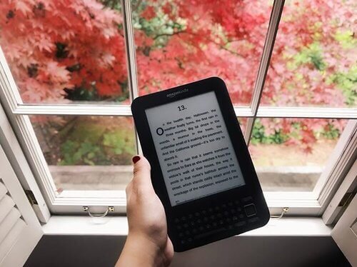 The Dreamers by Karen Thompson Walker is displayed on a kindle. A page from the book is visible against a window.