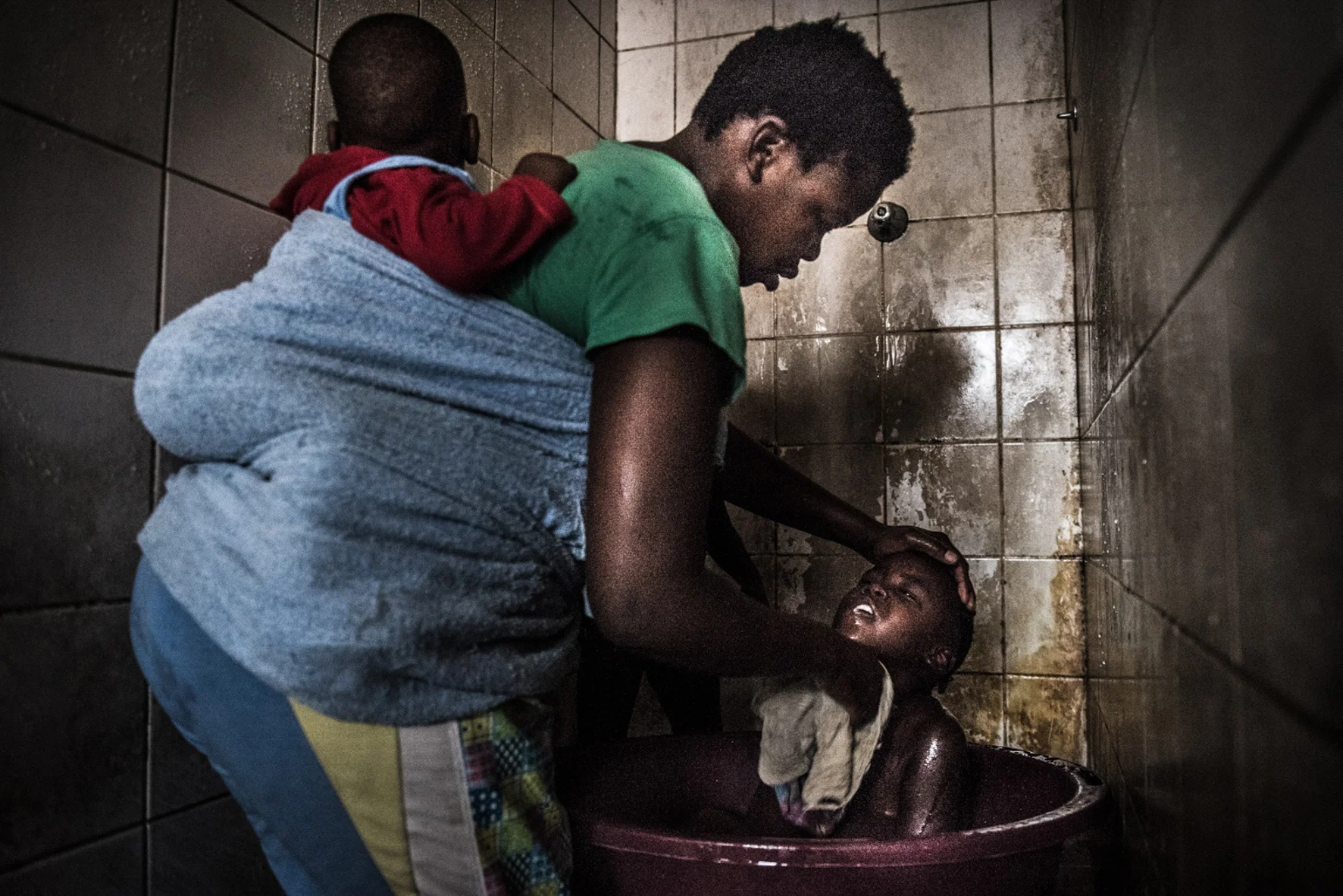  Busi is washing her children in one of the shower booth in the building. There is just cold water, and many of the toilets in the room don't work, so the place stinks of human feces 