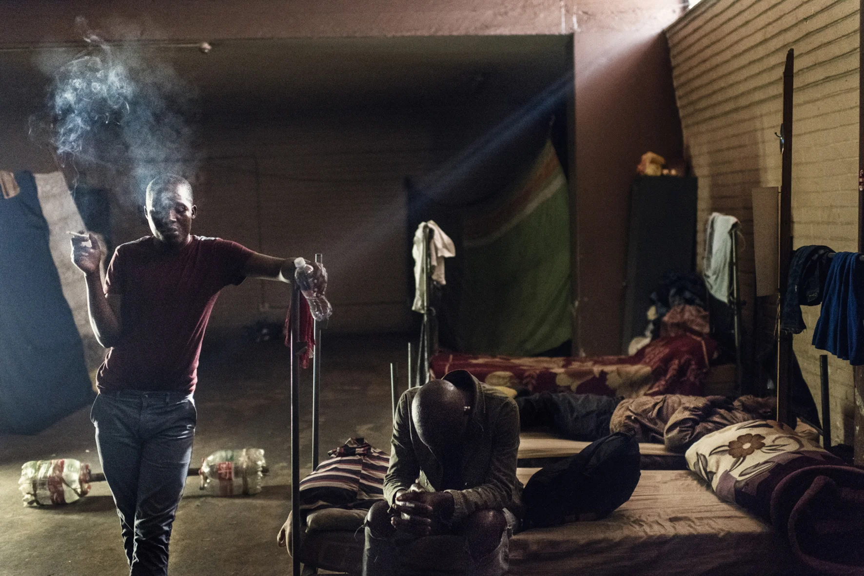  Ntokozo smoking a cigarette, trying to keep his head straight. In the back, two of hos friends are passed out. The weekends in Moth Building is filled with heavy drinking, and music playing from friday morning til' monday 