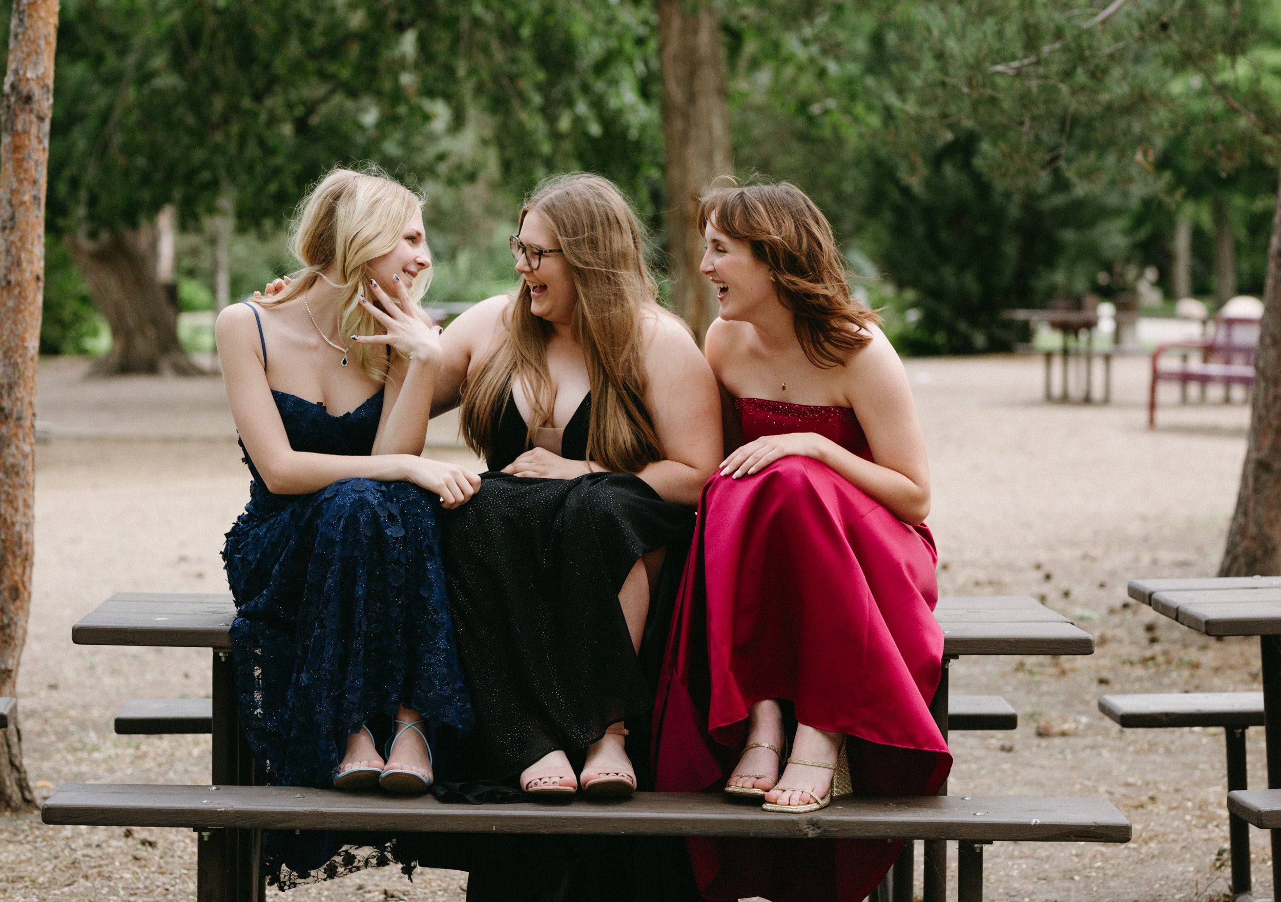  3 girls in grad dresses sit on picnic table laughing 