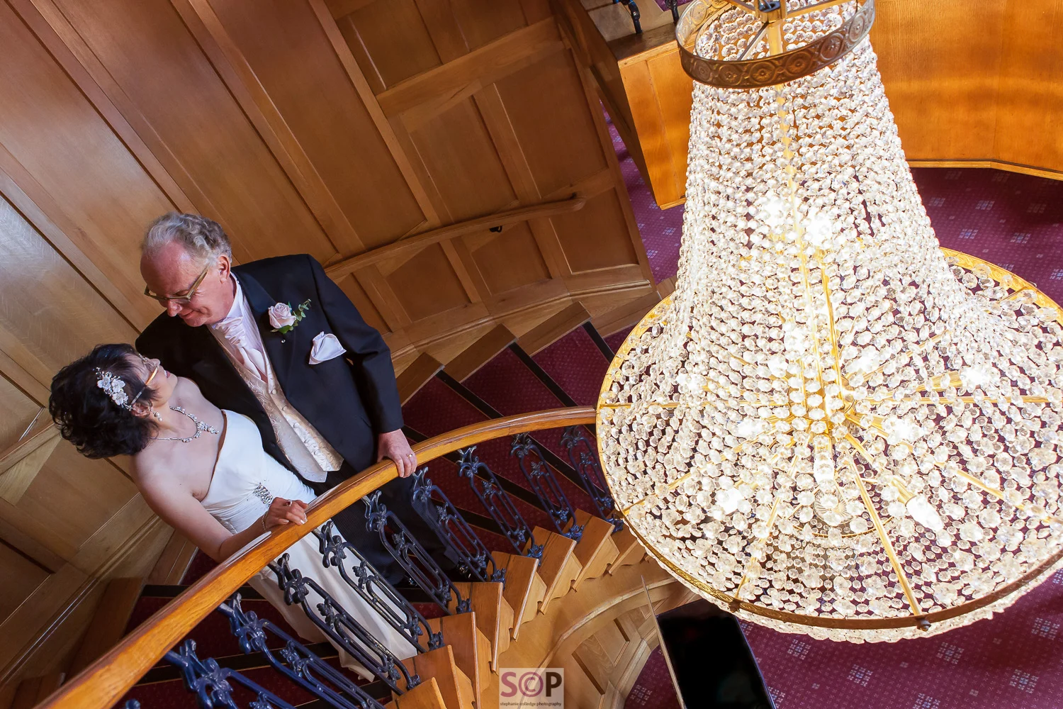 Bride and groom on the stairs with chandelier at Manor Hotel in Meriden