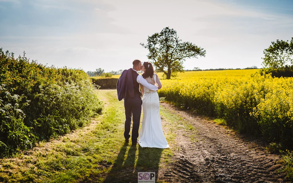 beautiful bride and groom kissing on a track by yellow rapeseed field.jpg