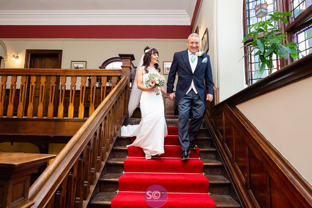 bride and father on the stairs laughing on the way to the service at the iliffe, coventry