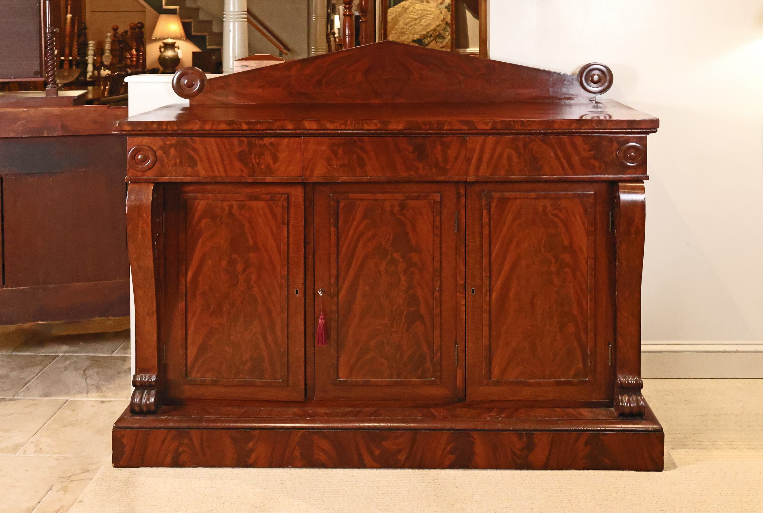 English Regency Sideboard in Flame Mahogany, 3 Drawers over 3 Cupboard Doors on Plinth Base, Flanked by Bell Flower Carved Scroll Pillars terminating in Decorative Curls</p> SKU: AB052024<p> </p><p>