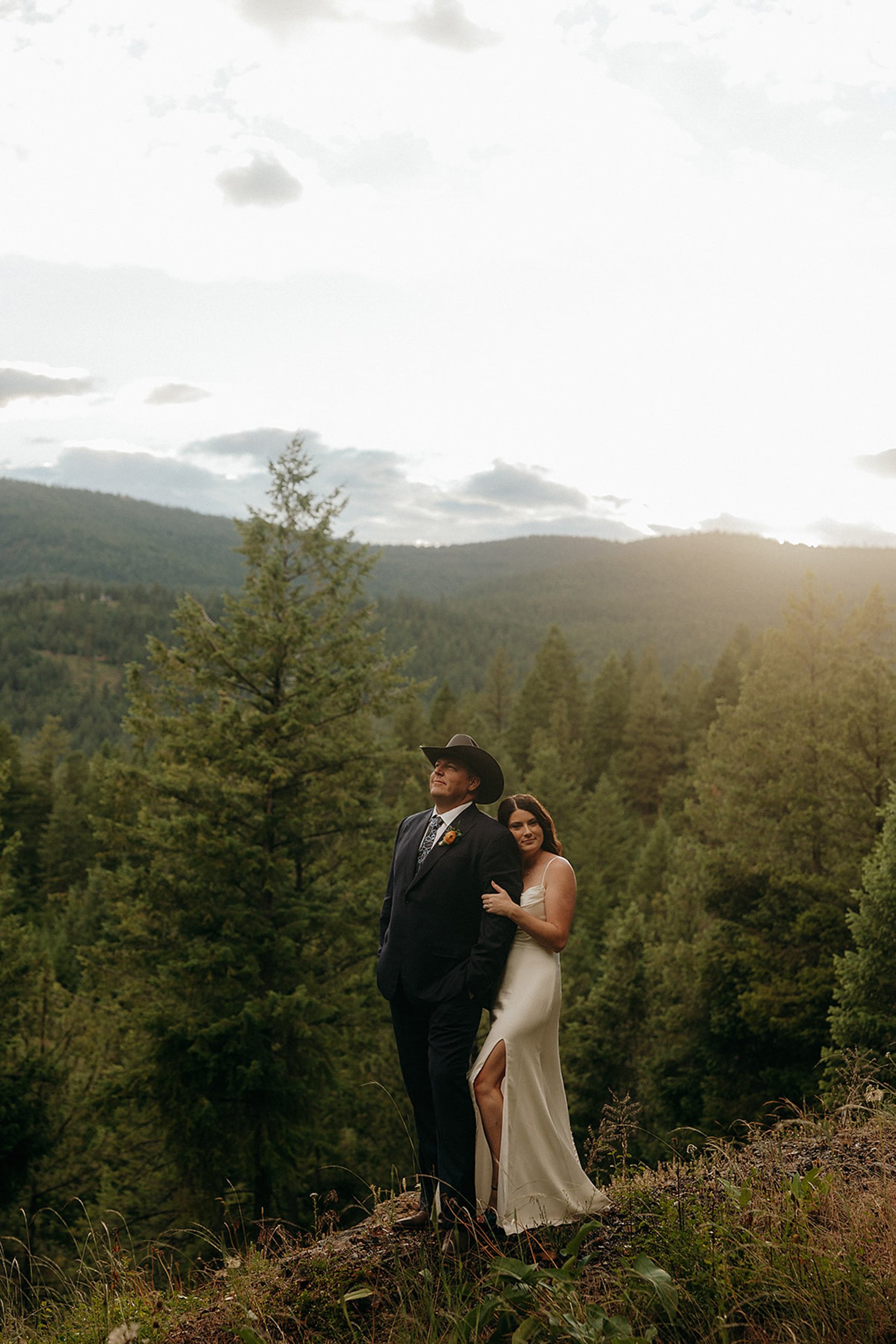 bride and groom embrace in front of trees and mountains