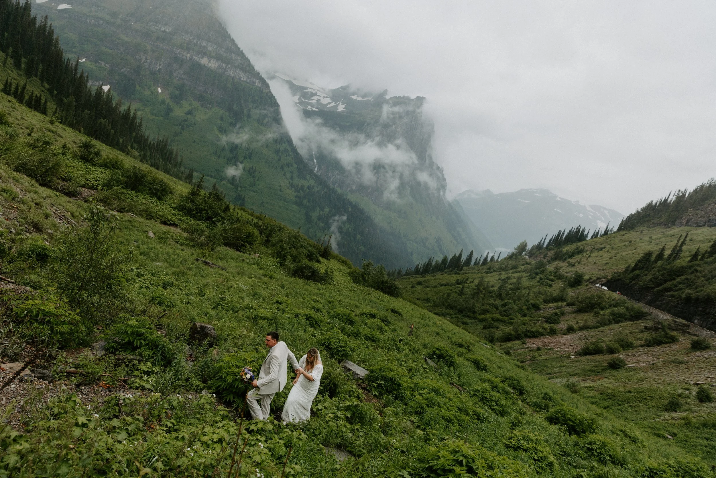 Bride and groom walk up the trail on a rainy day at Big Bend in Glacier National Park