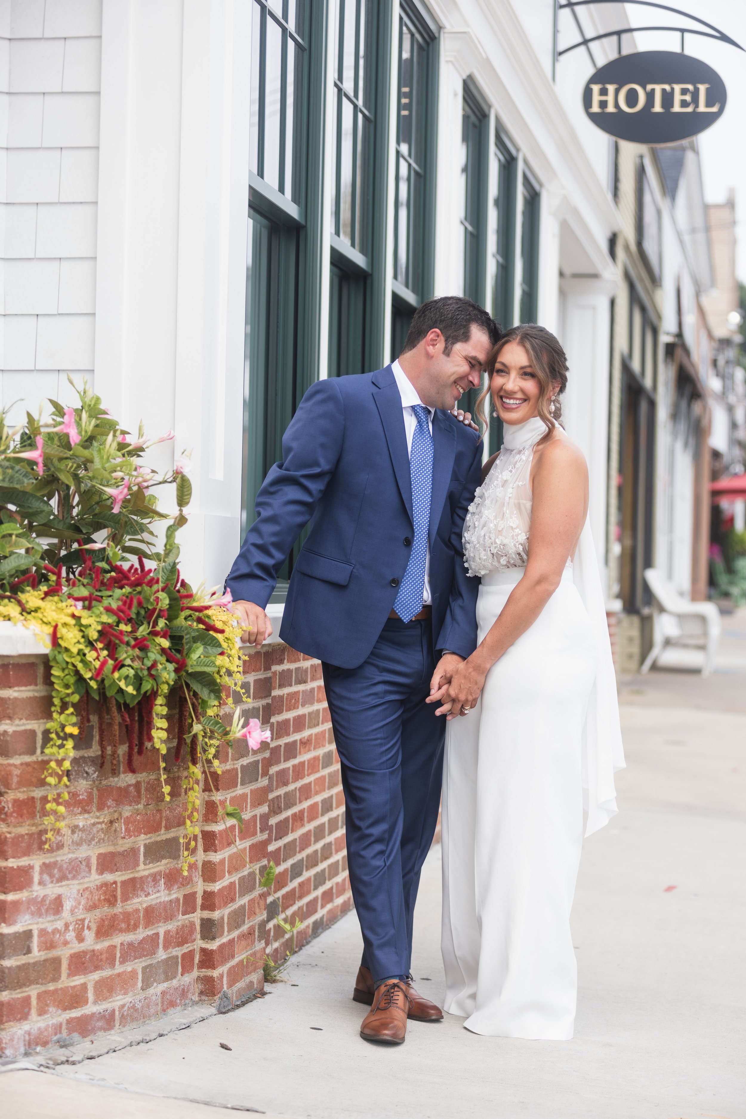 A happy man and woman in wedding attire sharing a tender moment outside of a hotel, standing close together, smiling and holding hands.
