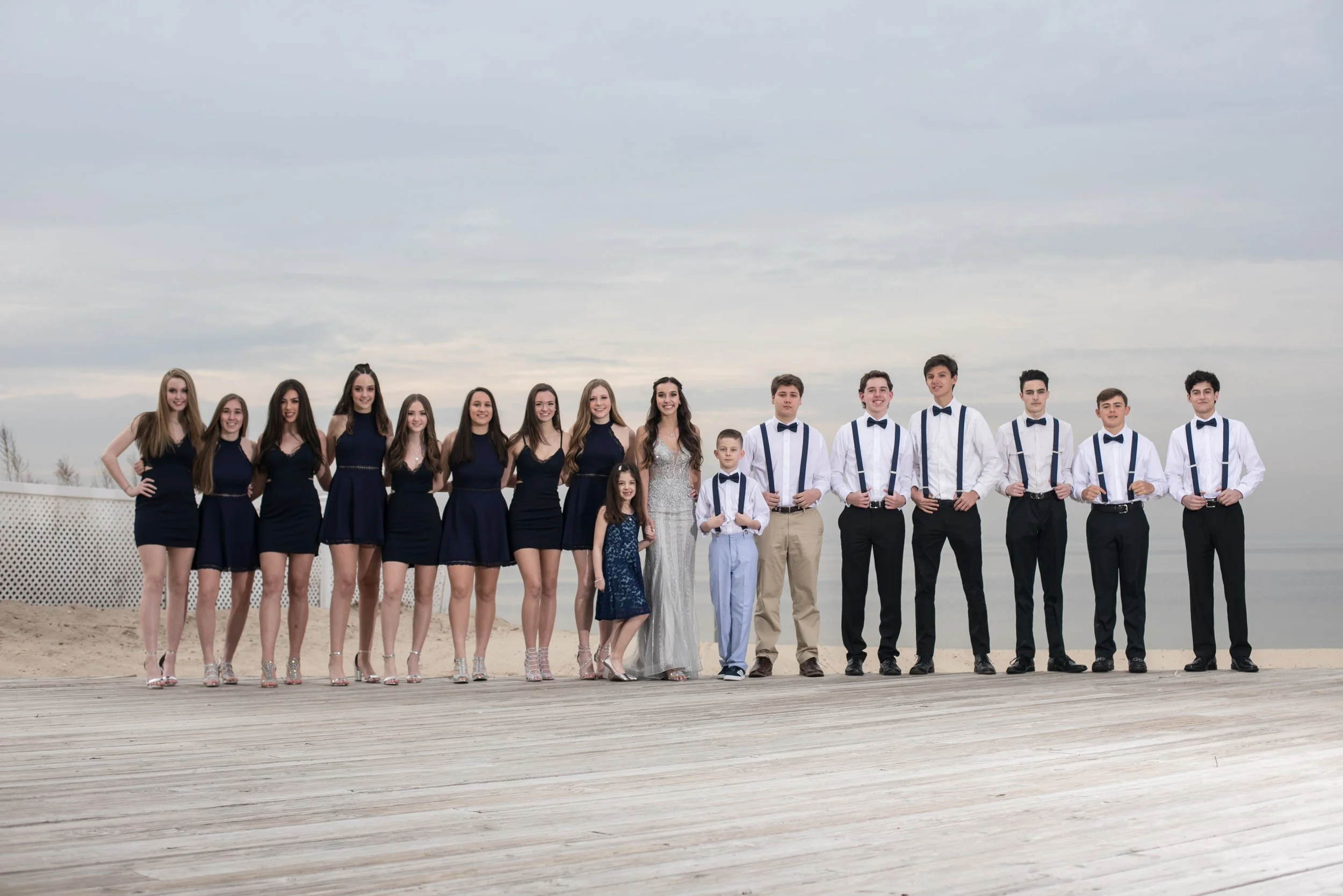 A group of teenagers dressed in formal attire standing side by side outdoors on a cloudy day.