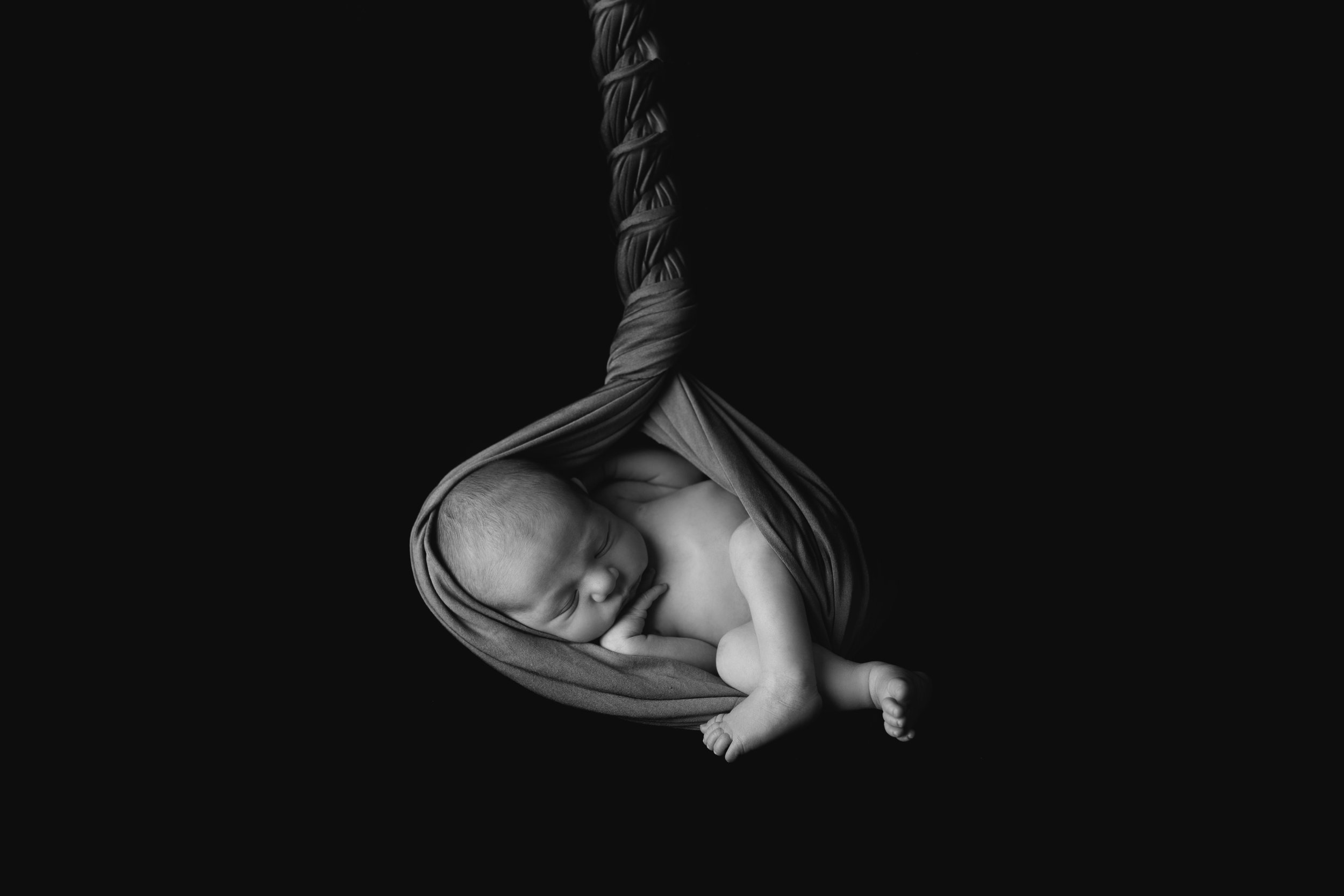 Black and white photo of a sleeping newborn baby wrapped in fabric, with delicate features and closed eyes.