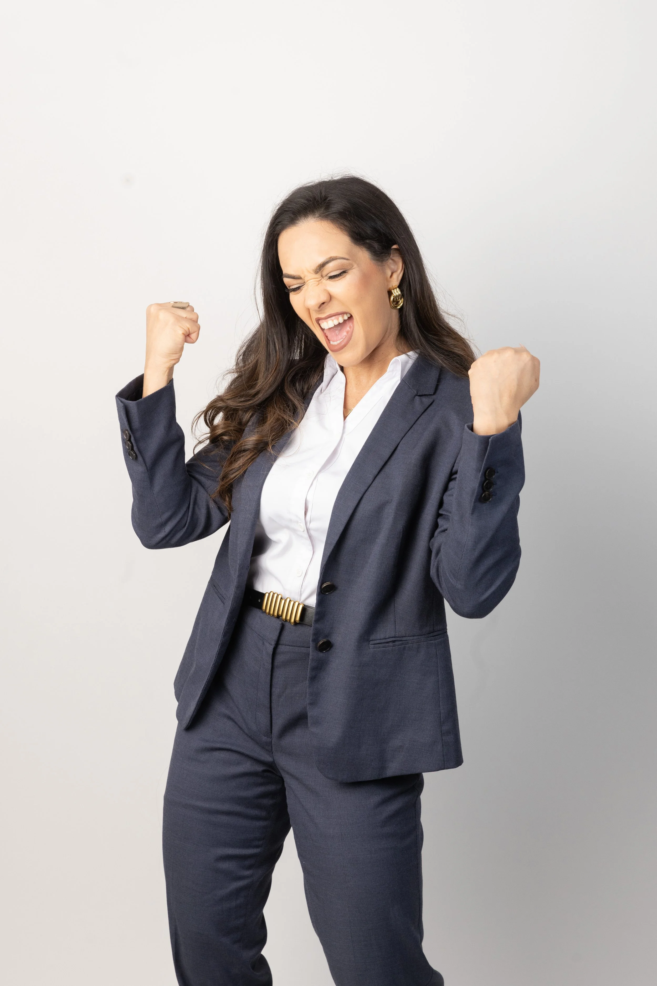 Woman in a business suit celebrating with clenched fists and a big smile.