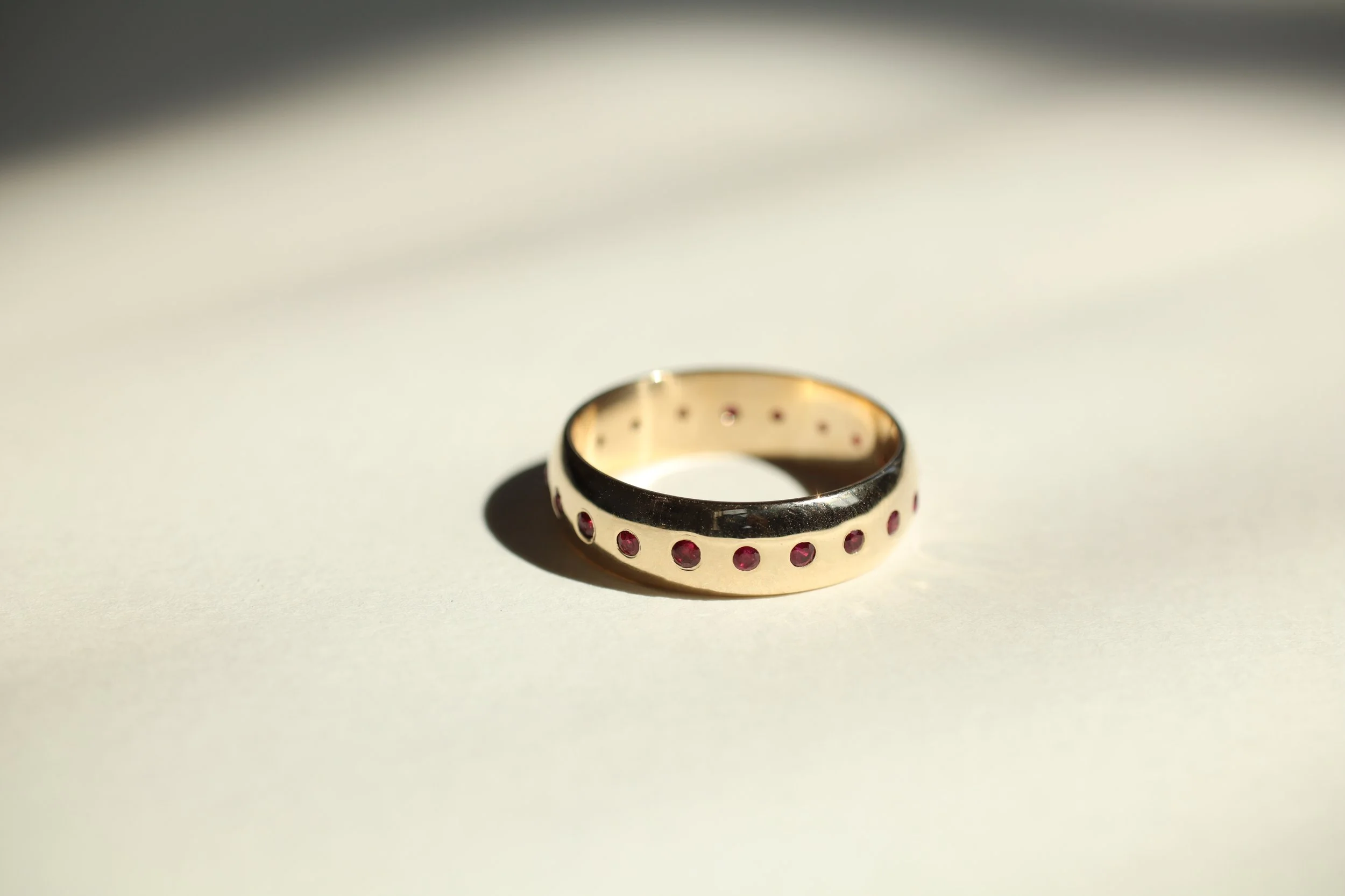 14k yellow gold wedding band for Josh with 20 flush-set rubies around the band.