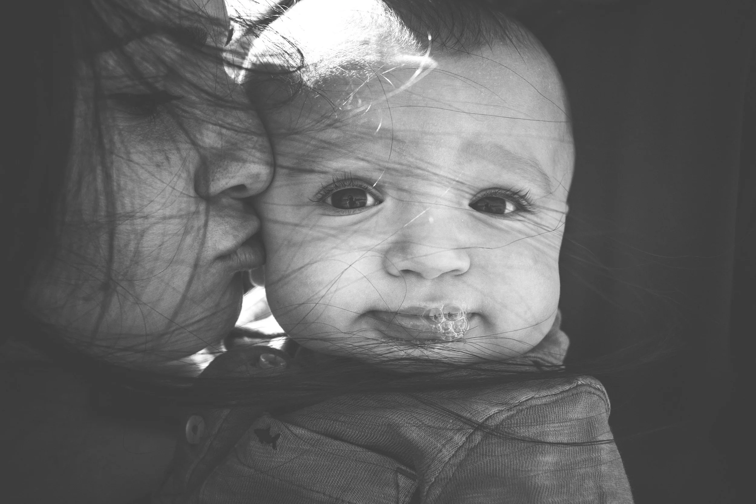 mom with wind blown hair kissing baby boy on cheek