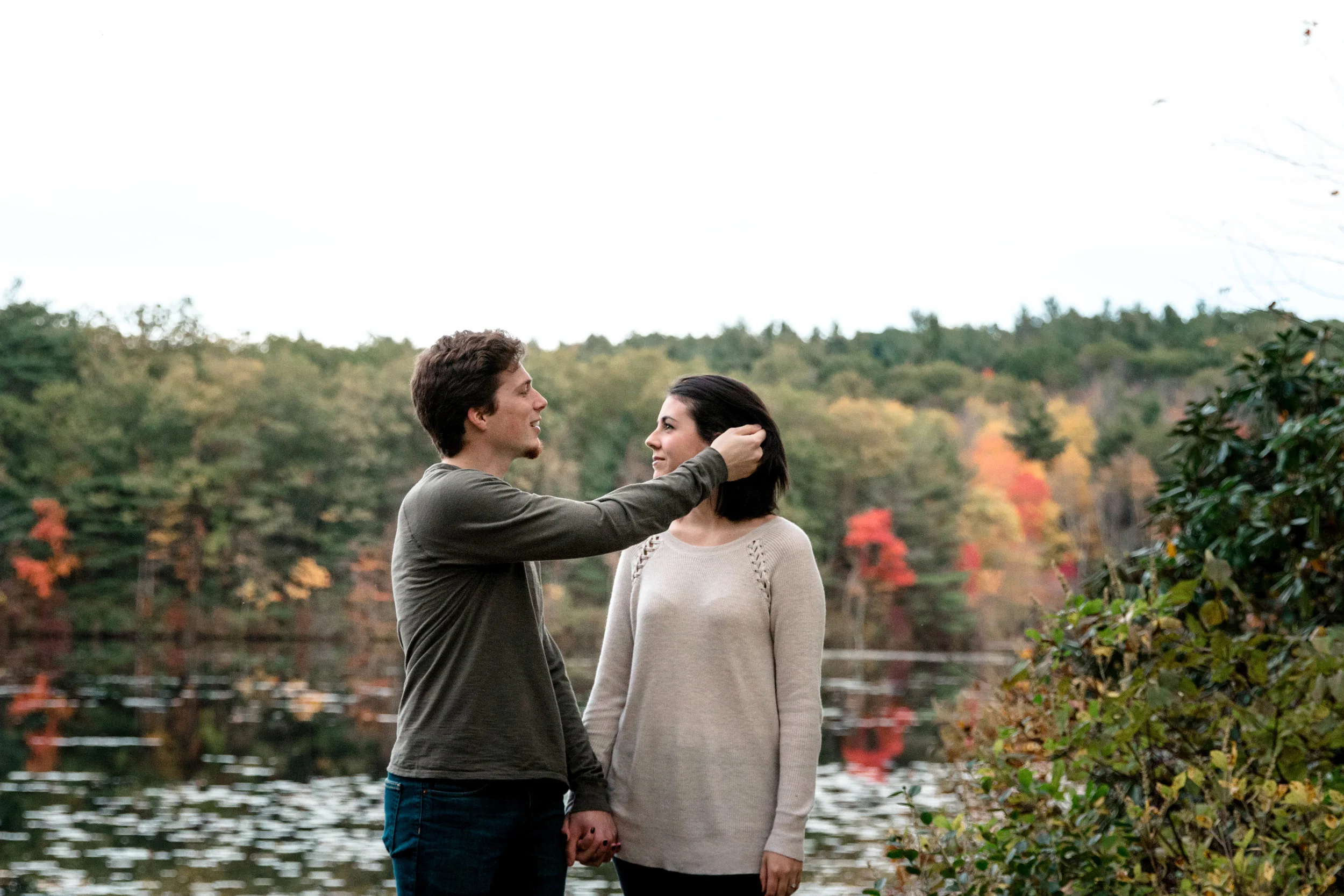 couple holding hands in front of fall foliage