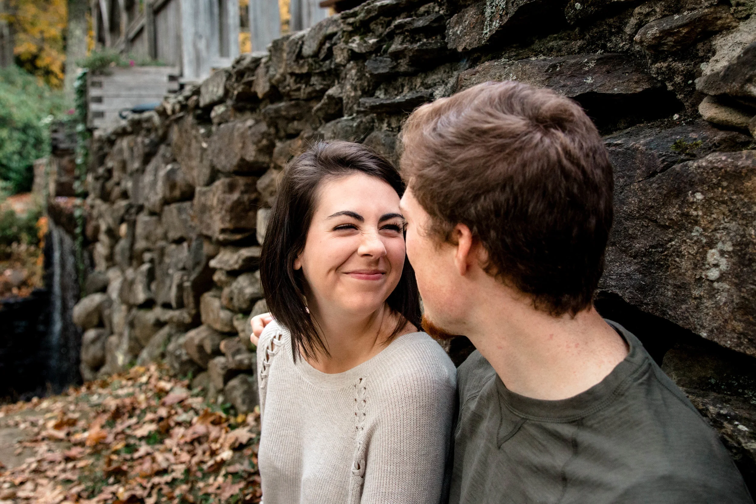 bride smiling at fiancé in front of rock wall and waterfall