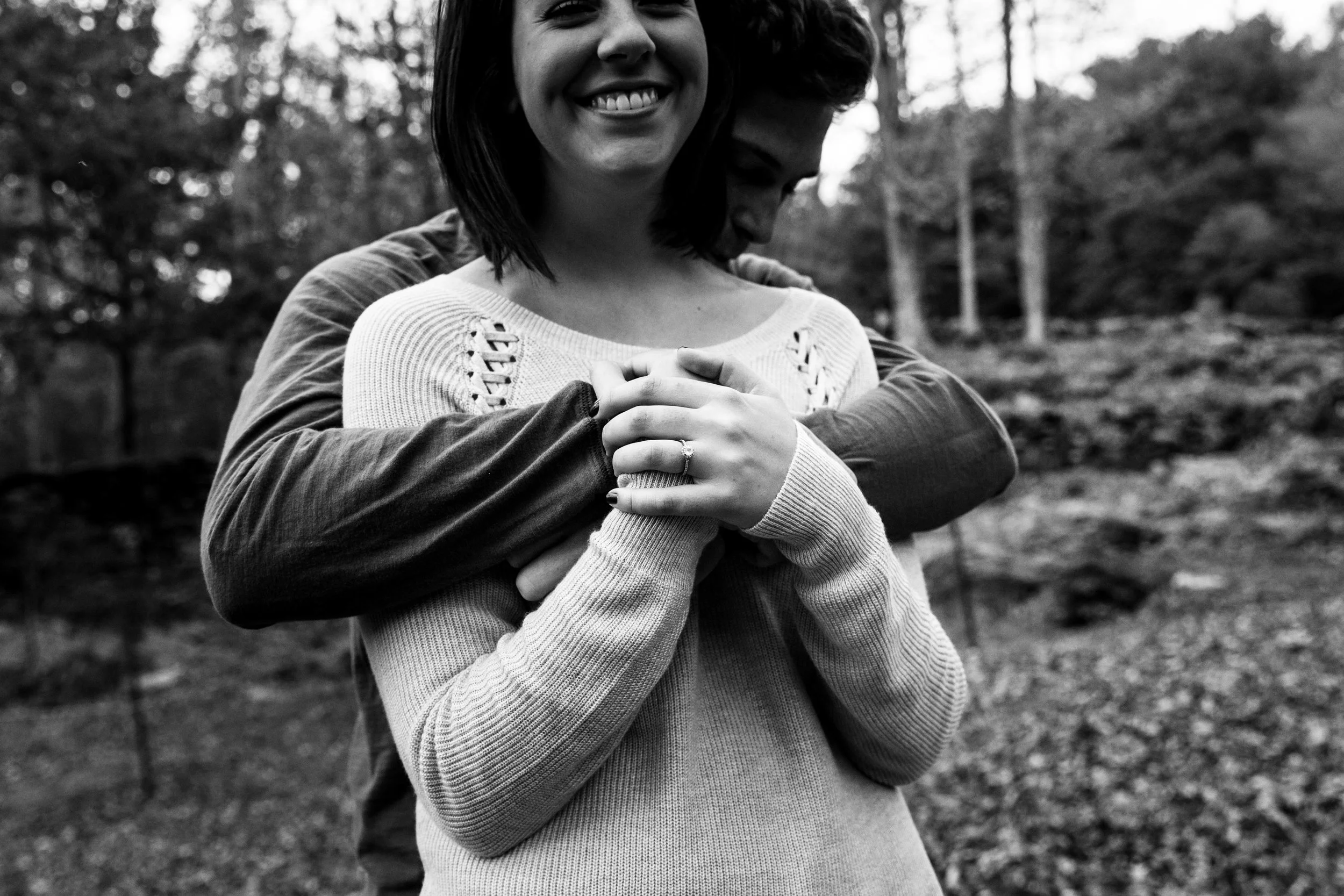 man hugs fiancé from behind in black and white