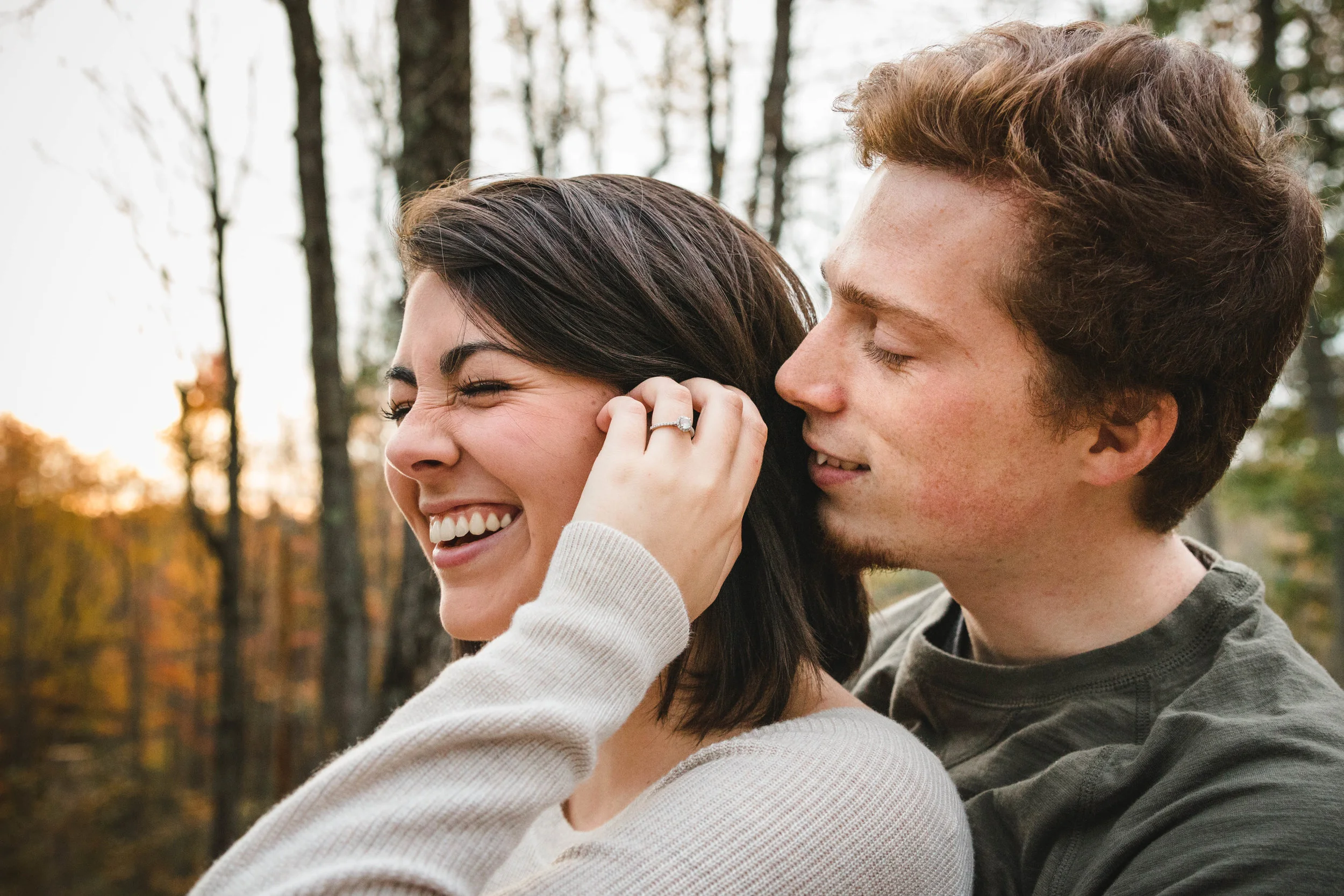 bride to be laughing and tucking back hair with fiancé and golden sunset