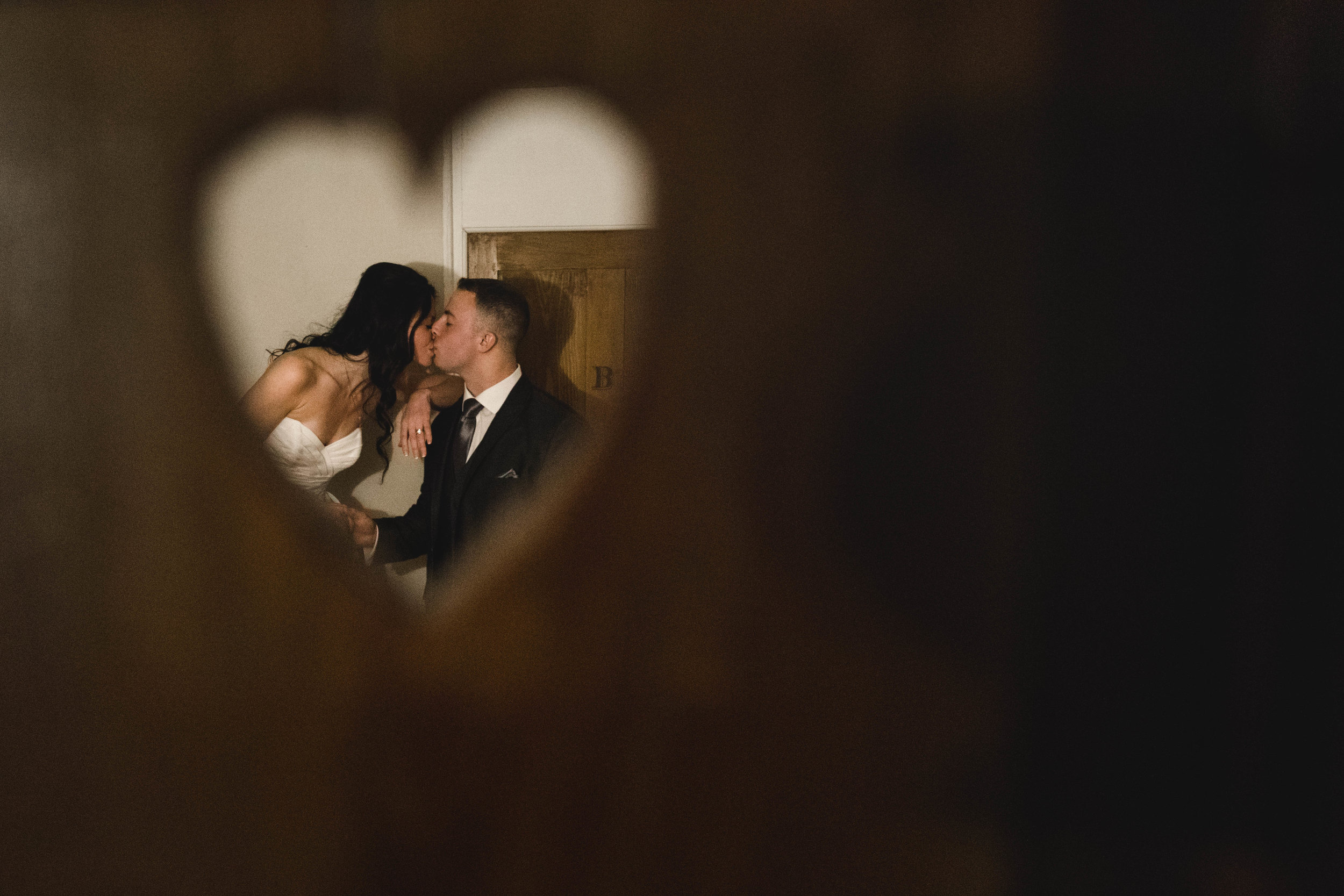 bride and groom kissing through heart shaped hole