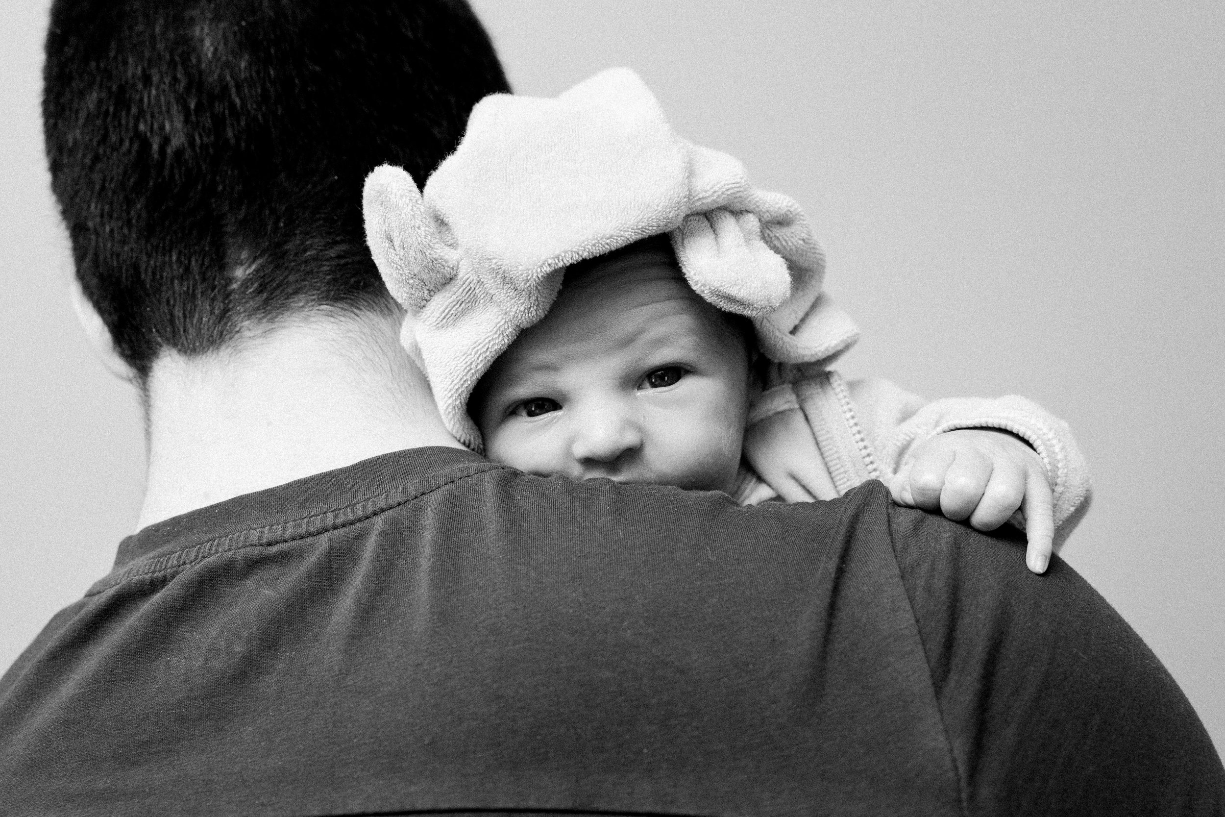 black &amp; white photo of baby looking at camera over dads shoulder