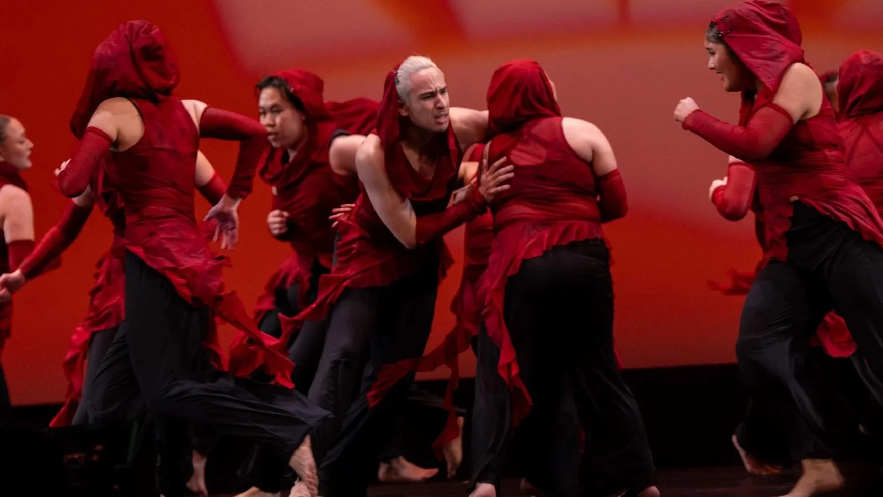 Group of dancers wearing red and black costumes performing on stage.