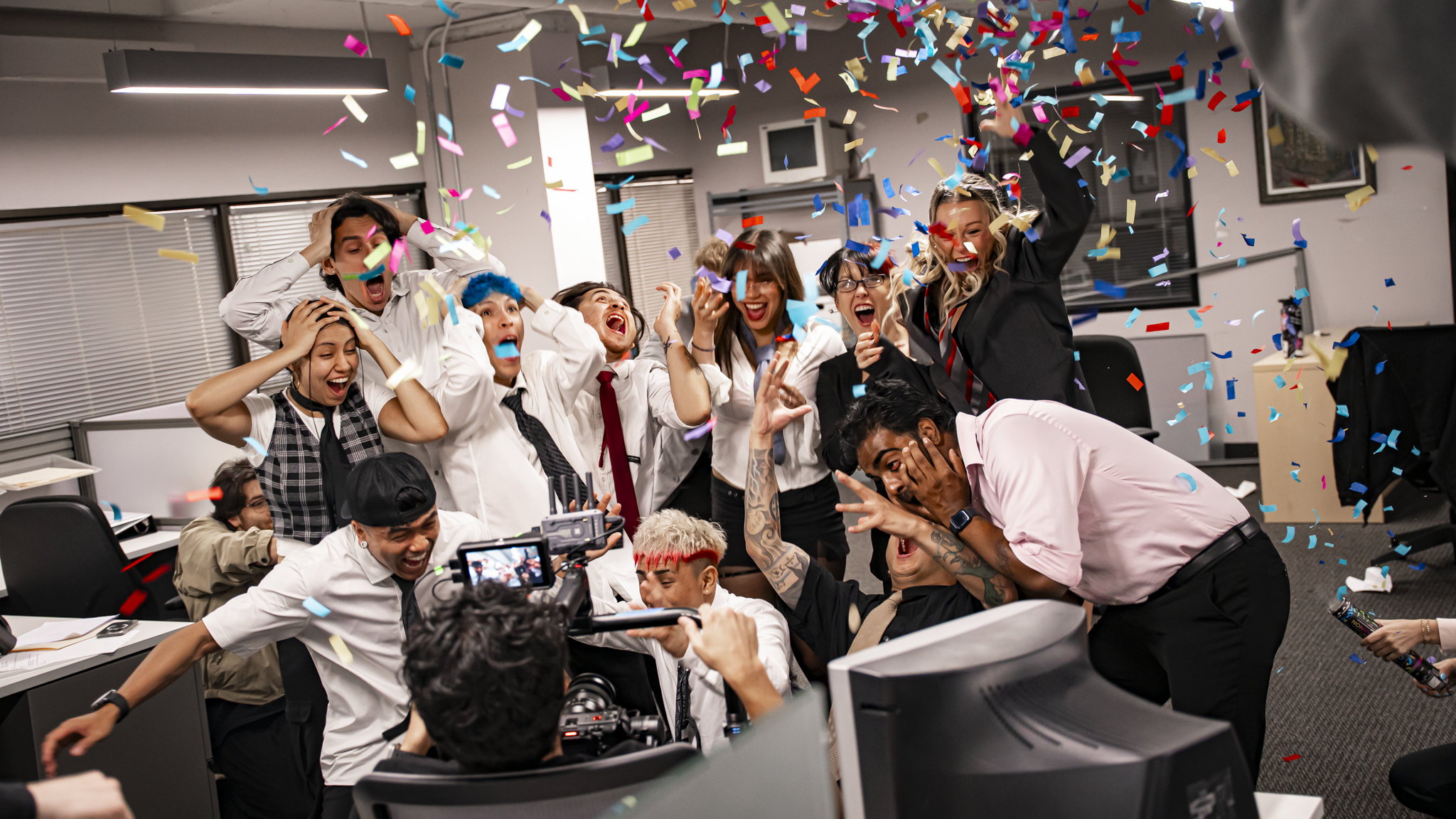 Group of diverse people celebrating in an office, throwing colorful confetti, smiling, and laughing.