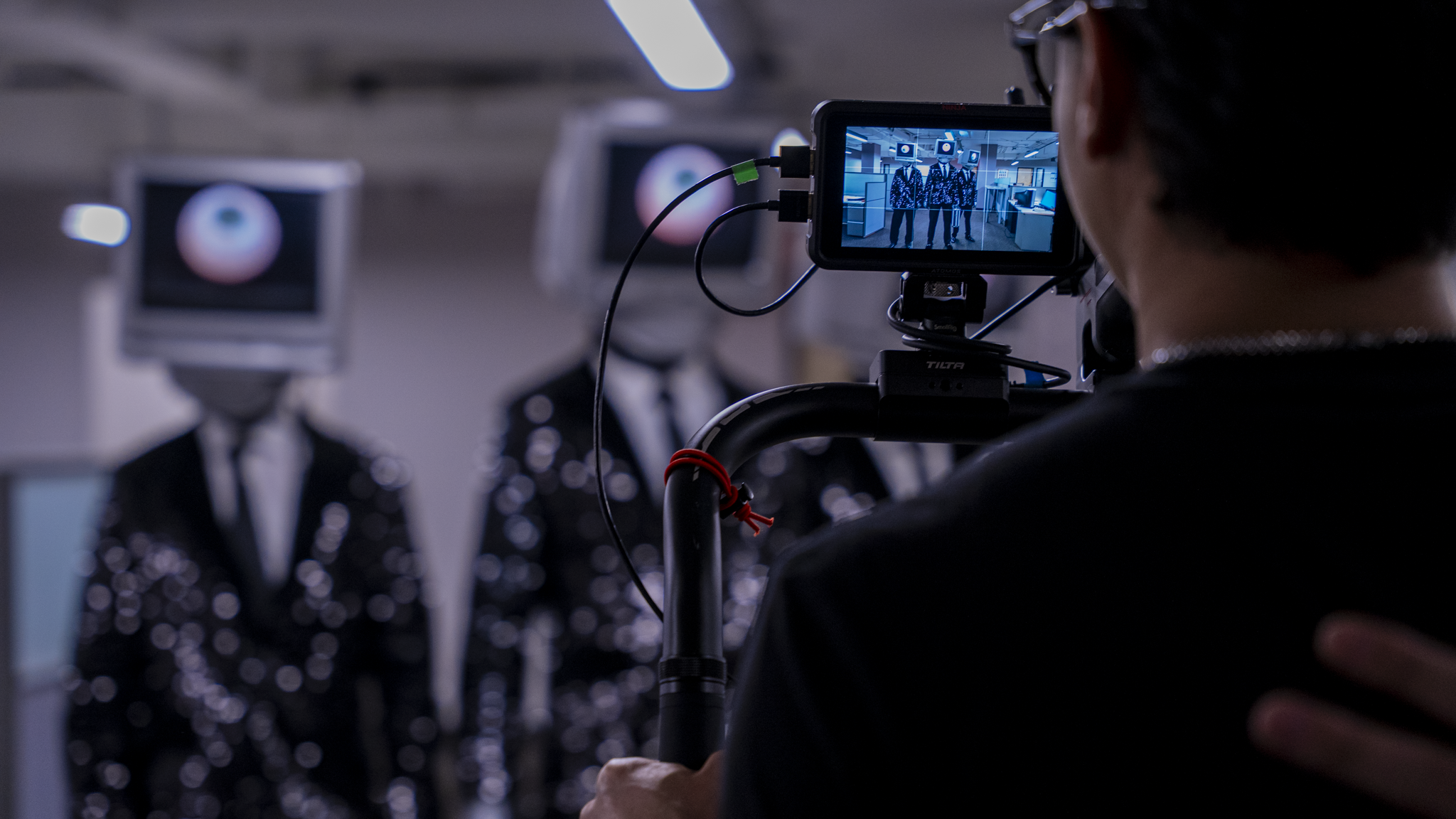 Behind-the-scenes of a fashion photo shoot, focusing on a photographer capturing models in tuxedos with eye-shaped patterns, using professional camera equipment in an indoor studio.