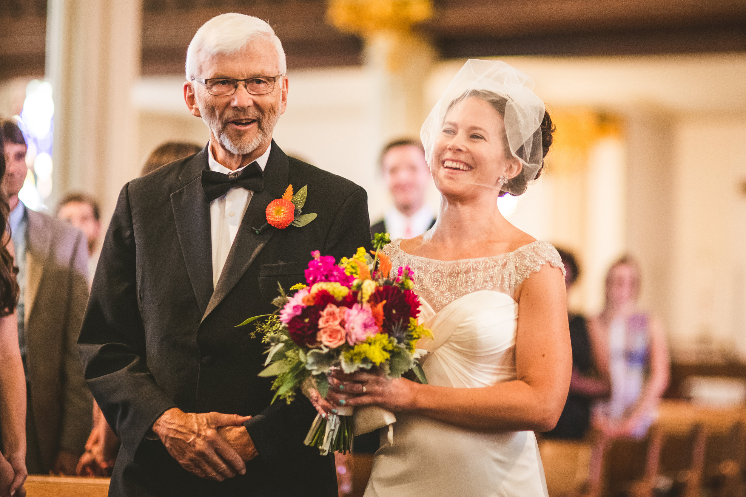 Bride holding vibrantly colored bouquet with her father at her side wearing an orange boutonniere