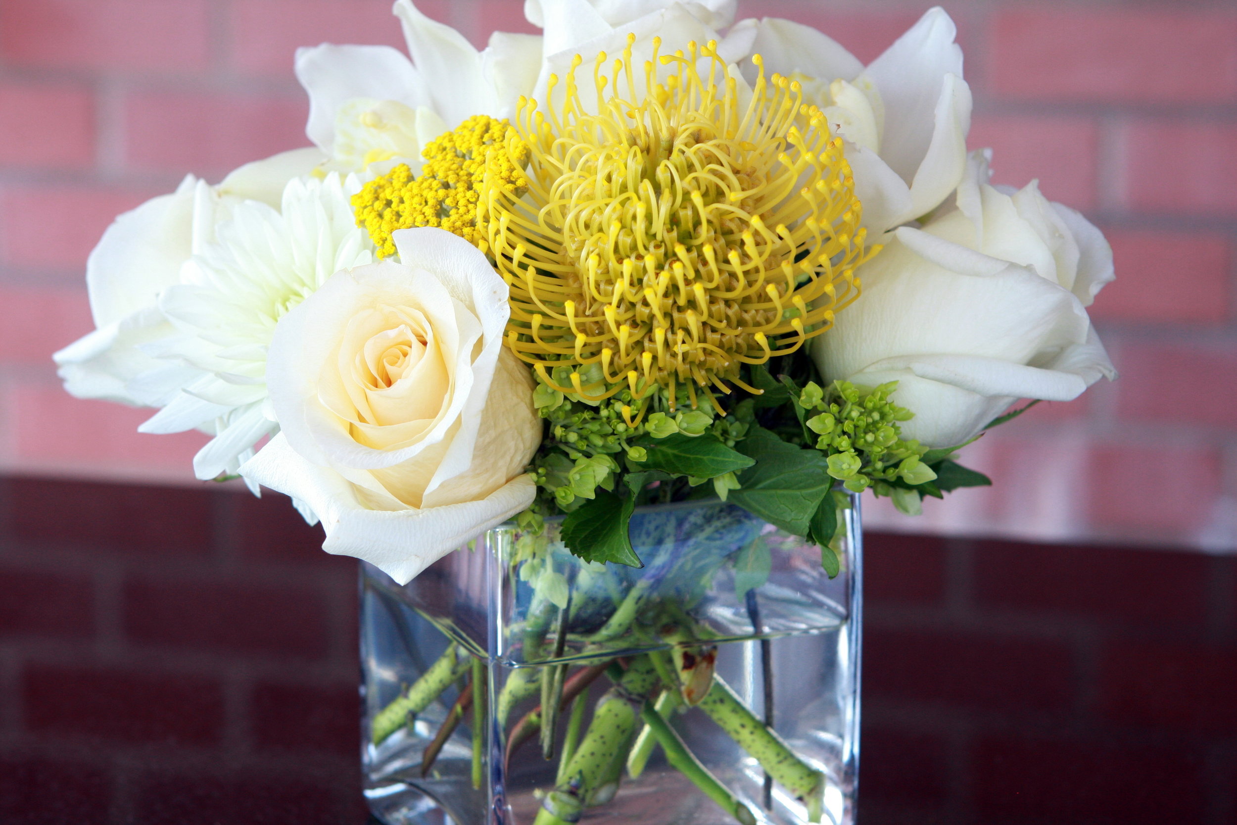 Square glass vase holding white roses and a yellow nodding pincushion flowers.