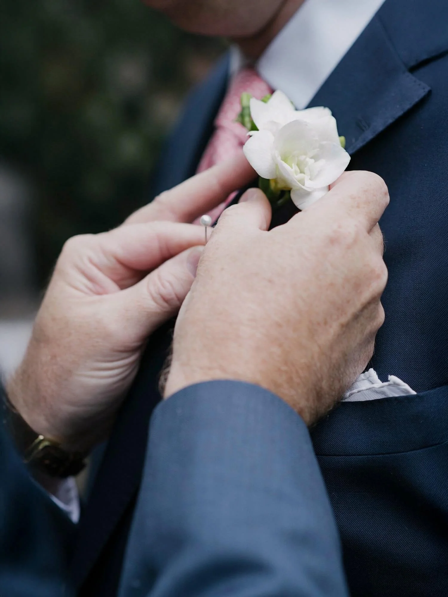 Close up of two hands pinning a white boutonnière on a man’s suit lapel