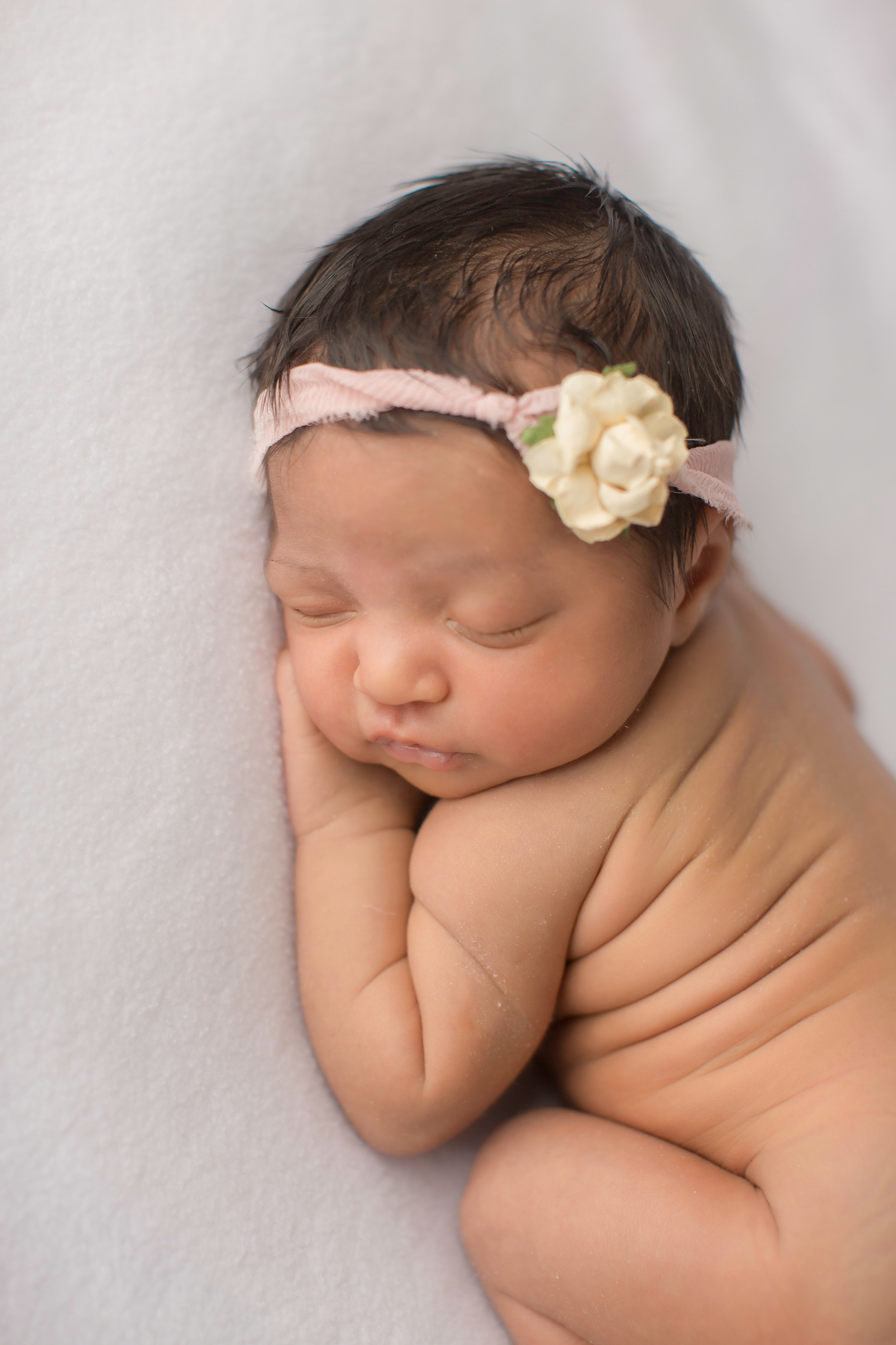  newborn baby girl cuddling up in grand blanc michigan with flower headband for pictures 