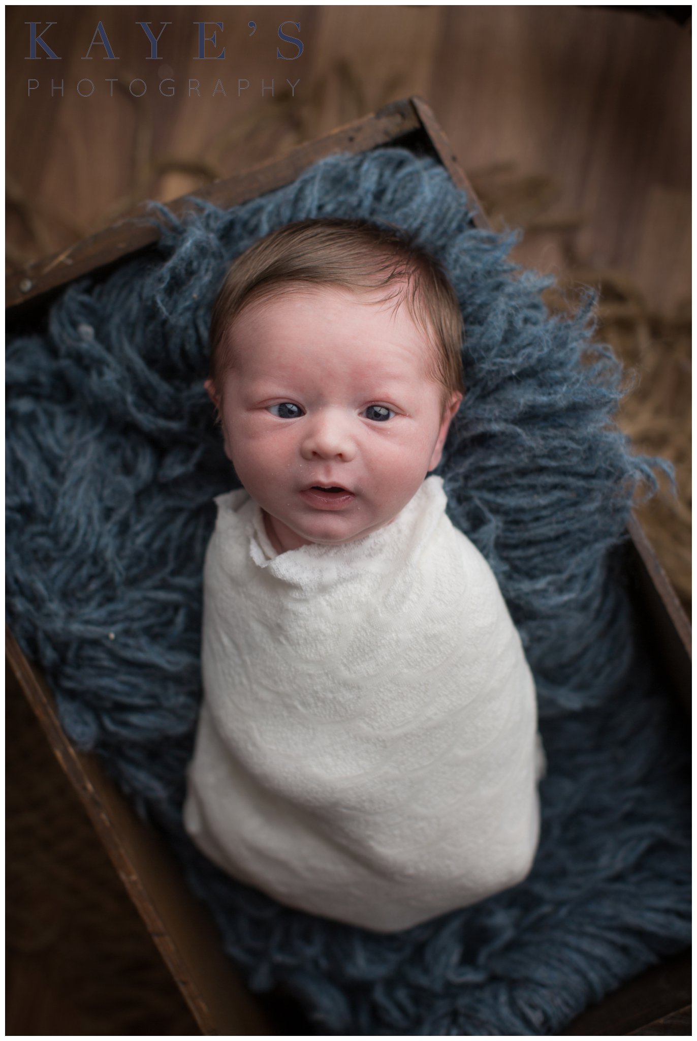 Baby boy in crate on blue rug with eyes wide open