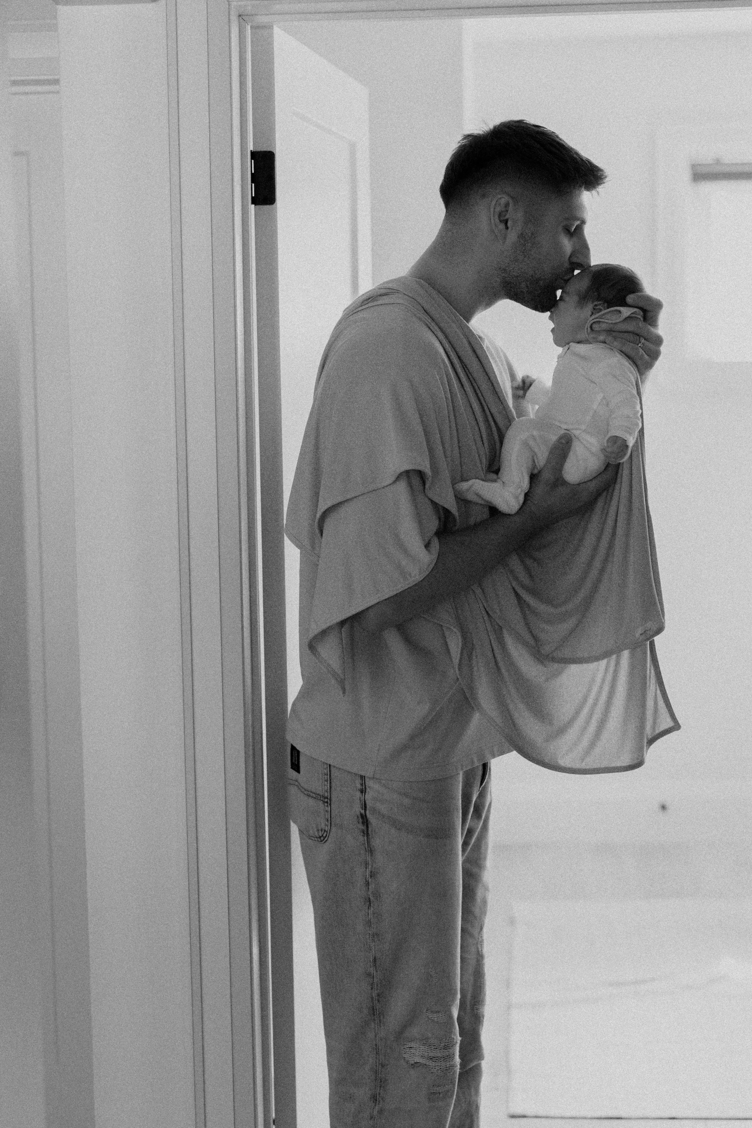 A man holding a baby and kissing them on the forehead in a hospital hallway.