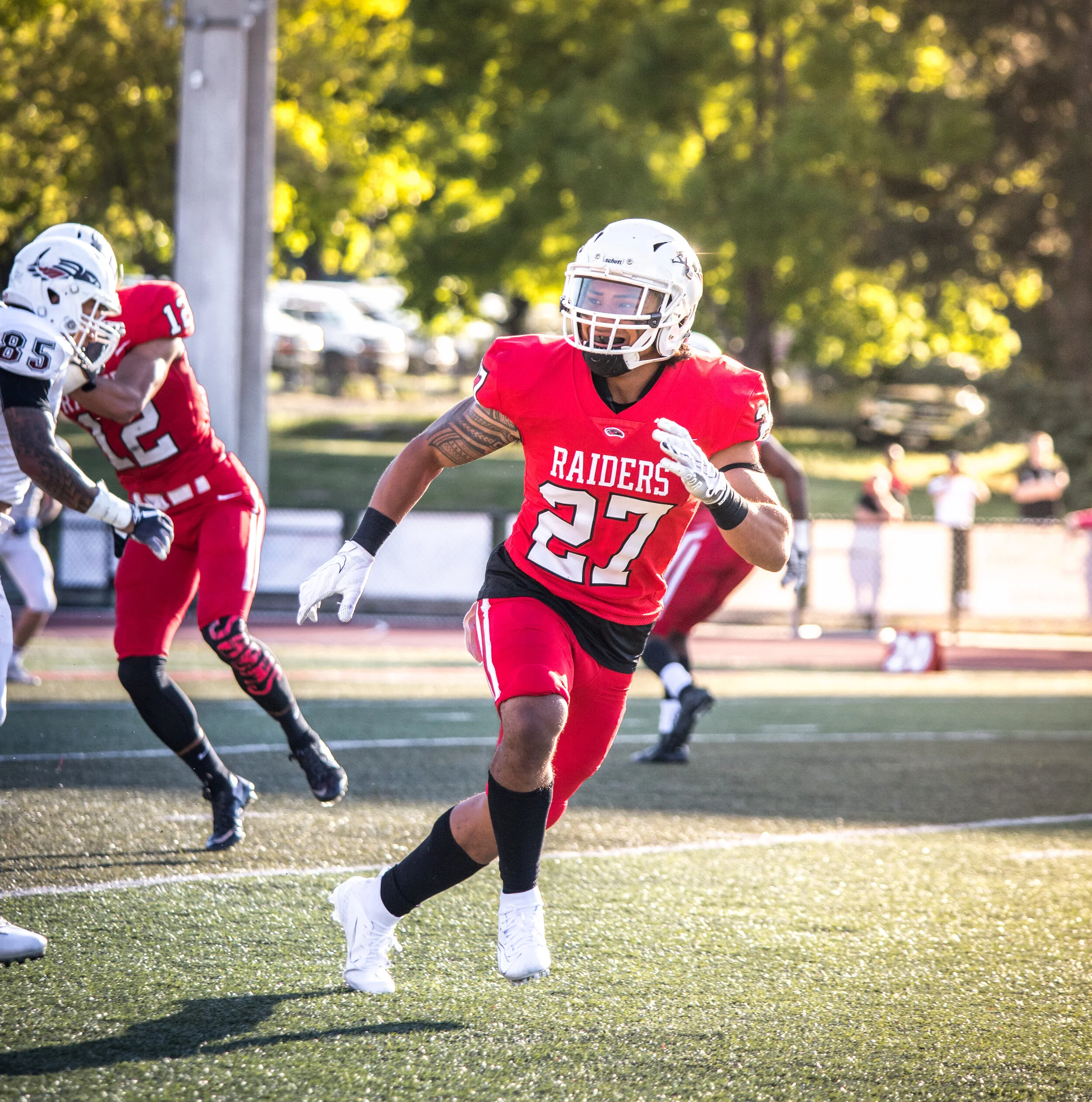 Football player in red and black uniform with number 27 and 'Raiders' on jersey running on the field during a game.