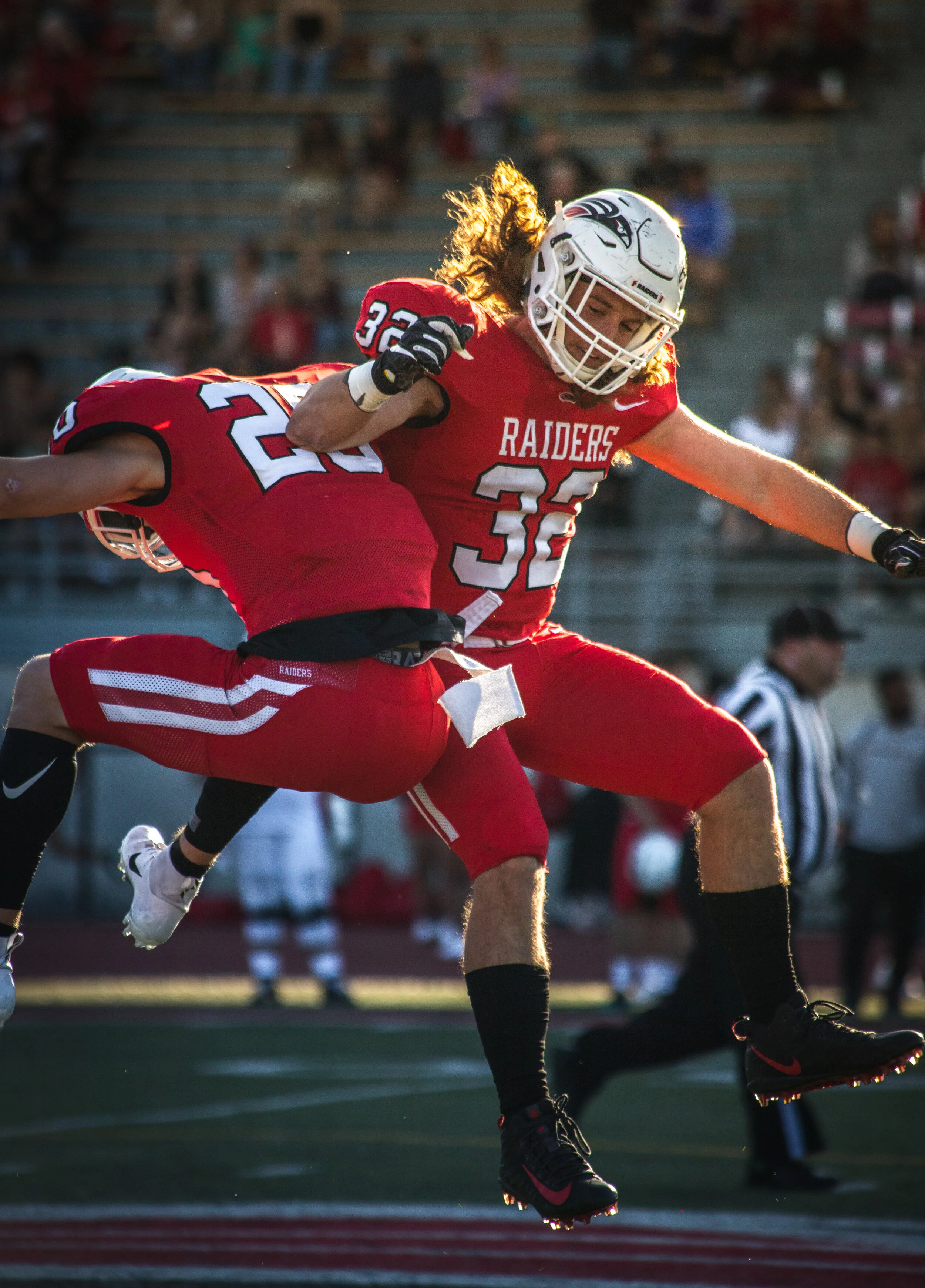 A football player wearing a red uniform with 'RAIDERS' and the number 36 is leaping in the air during a game, with another player in a similar uniform tackling him.