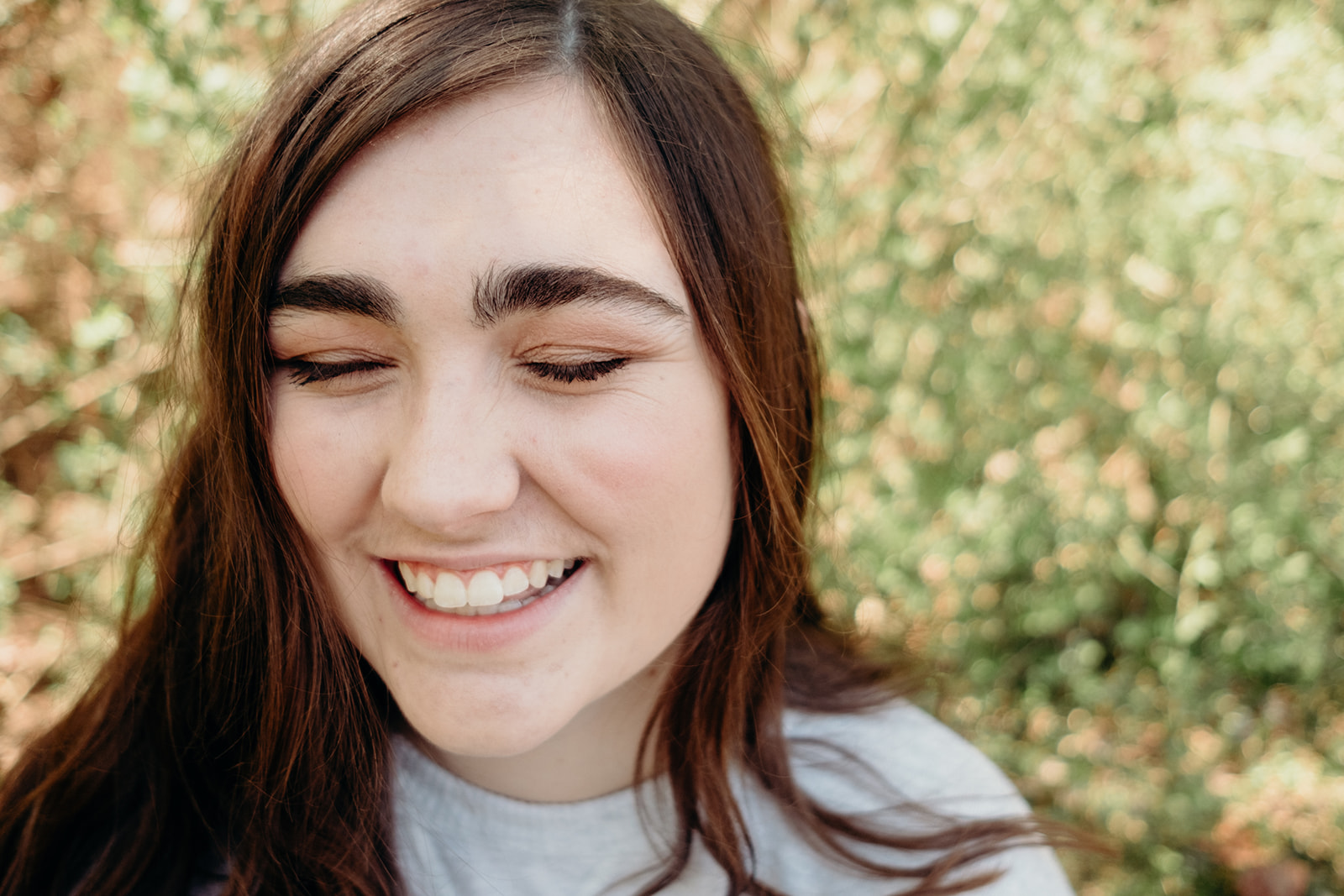 A girl laughs with her eyes closed during a senior portrait session in North Carolina. 
