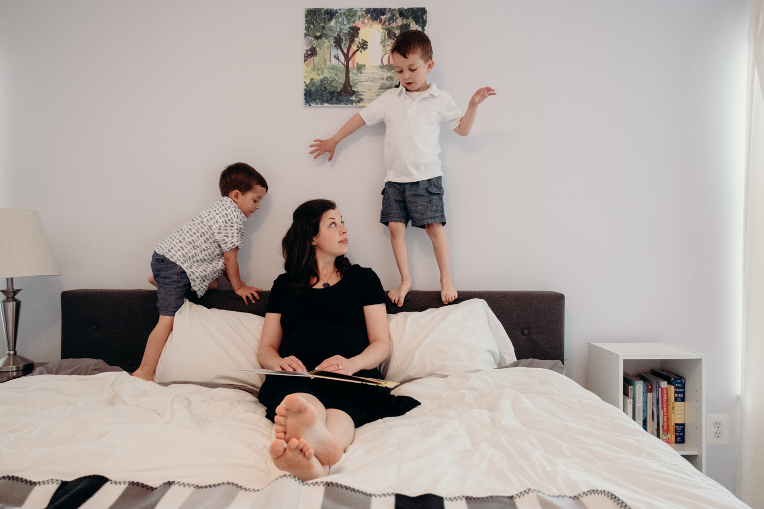 A mother tries to read a book to her sons while they climb all over her bed.