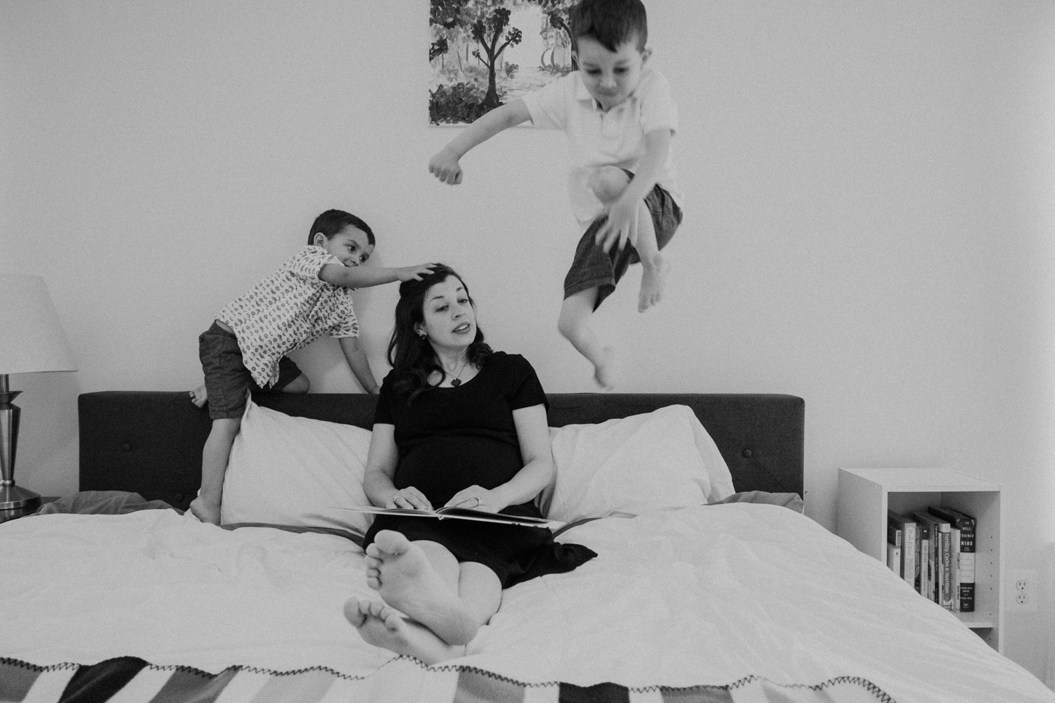 A boy jumps over his mother onto her bed while she looks on. 