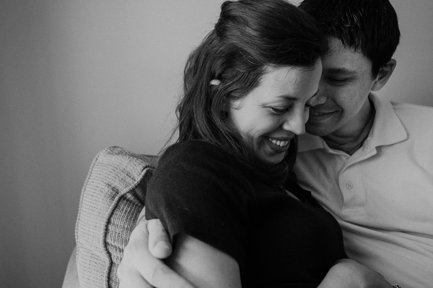 A husband snuggles with his pregnant wife in their home full of boys. 