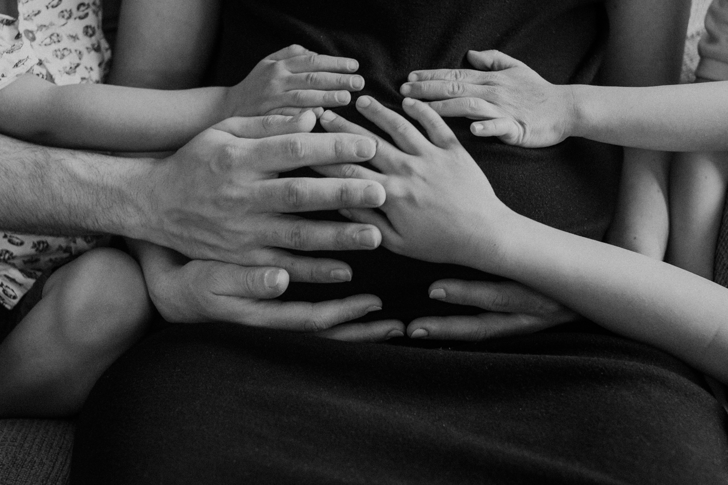 A father and his three sons place their hands on the belly of their pregnant mother. 