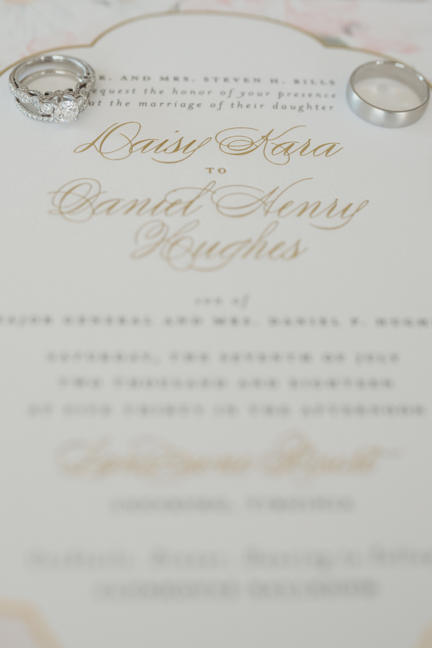 A couple's wedding rings sit on their wedding invitation.