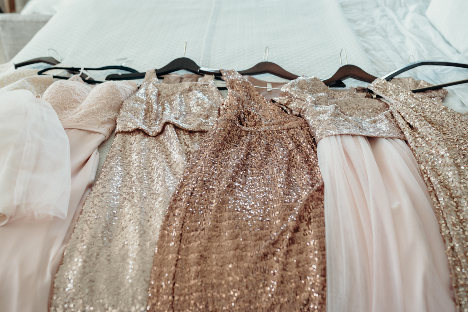 A slew of sparkly bridesmaids dresses wait on the bed before a wedding at Lansdowne Resort.