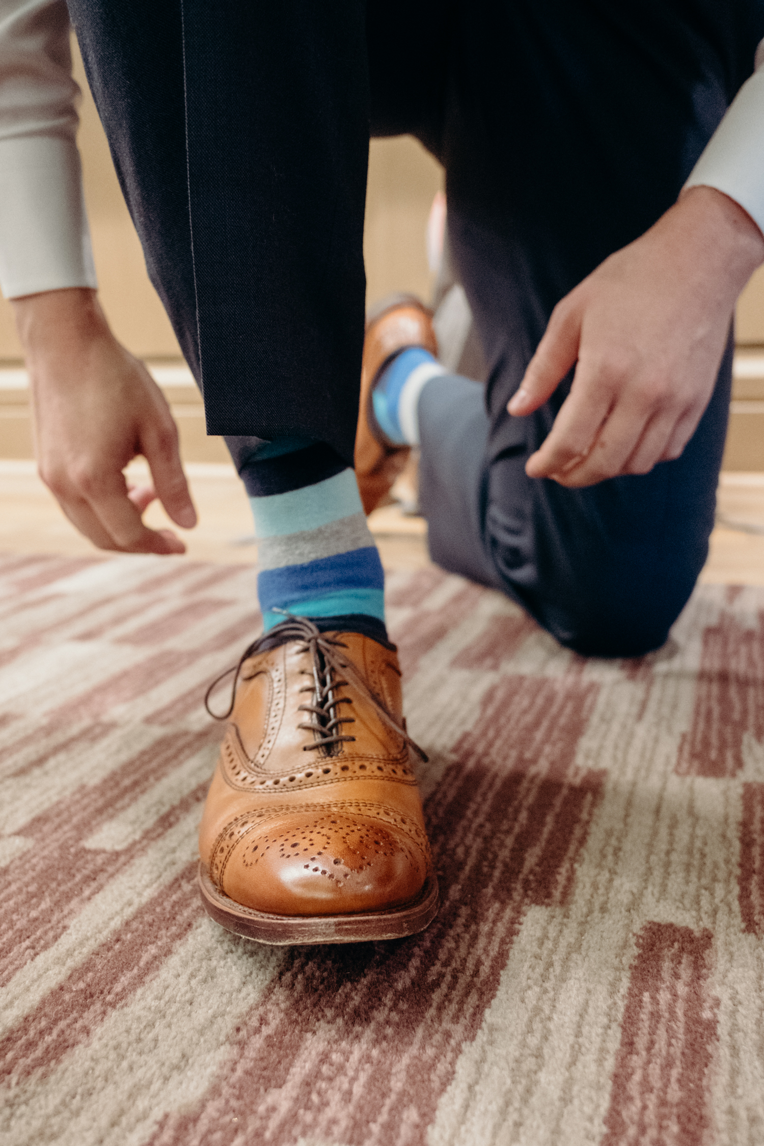 A groom with brown shoes and blue socks leans down to finish tying his shoes before his wedding at Lansdowne Resort.