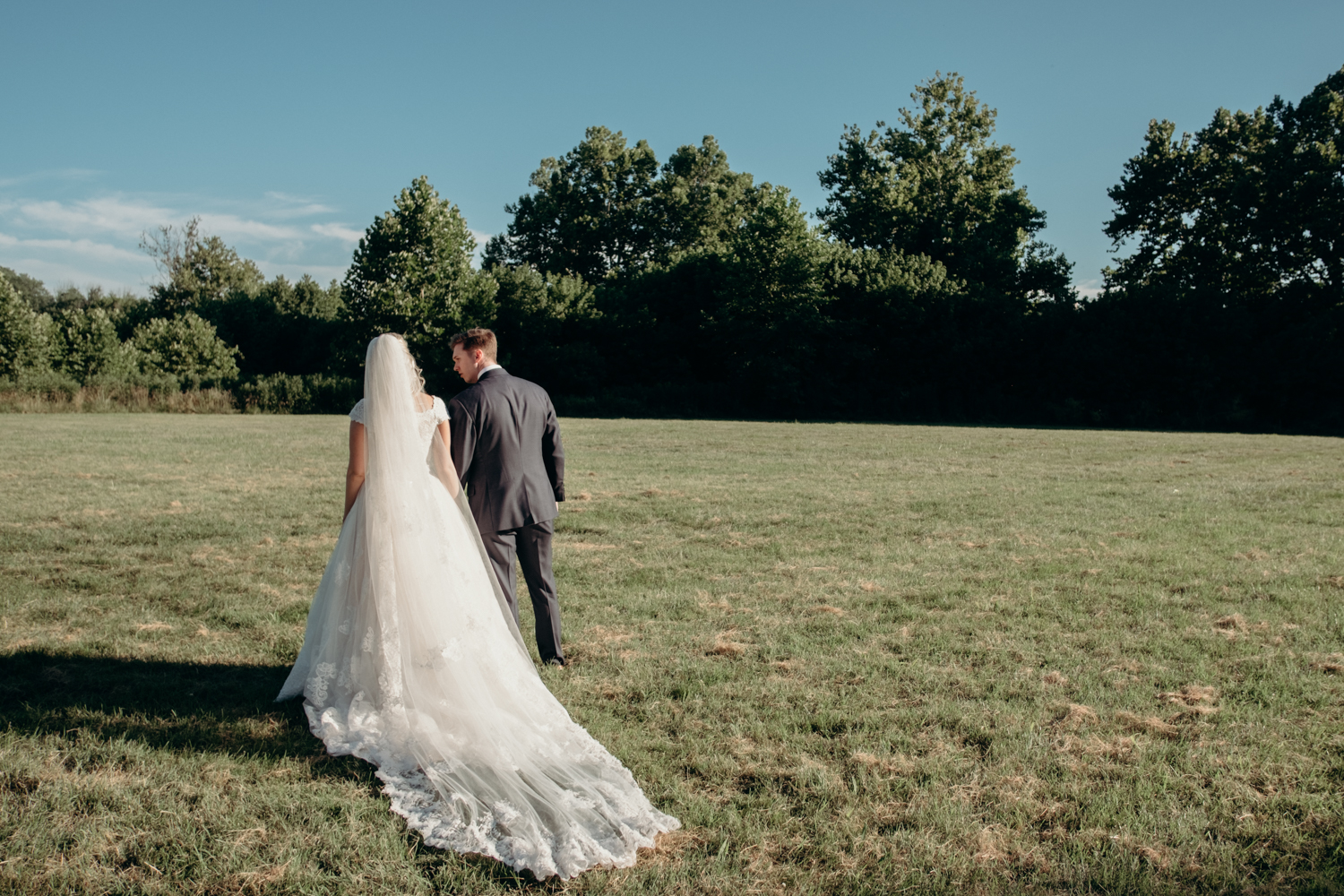 A husband and wife walk through a field in the sunshine after their outdoor wedding ceremony at Lansdowne Resort.