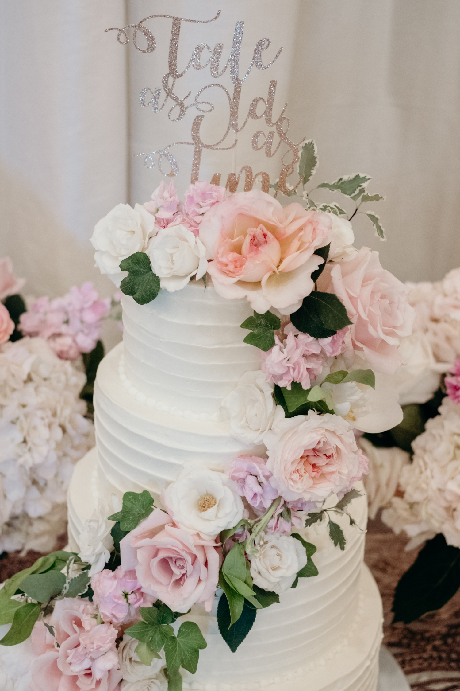 A three-tiered white wedding cake is adorned with pink and white flowers.