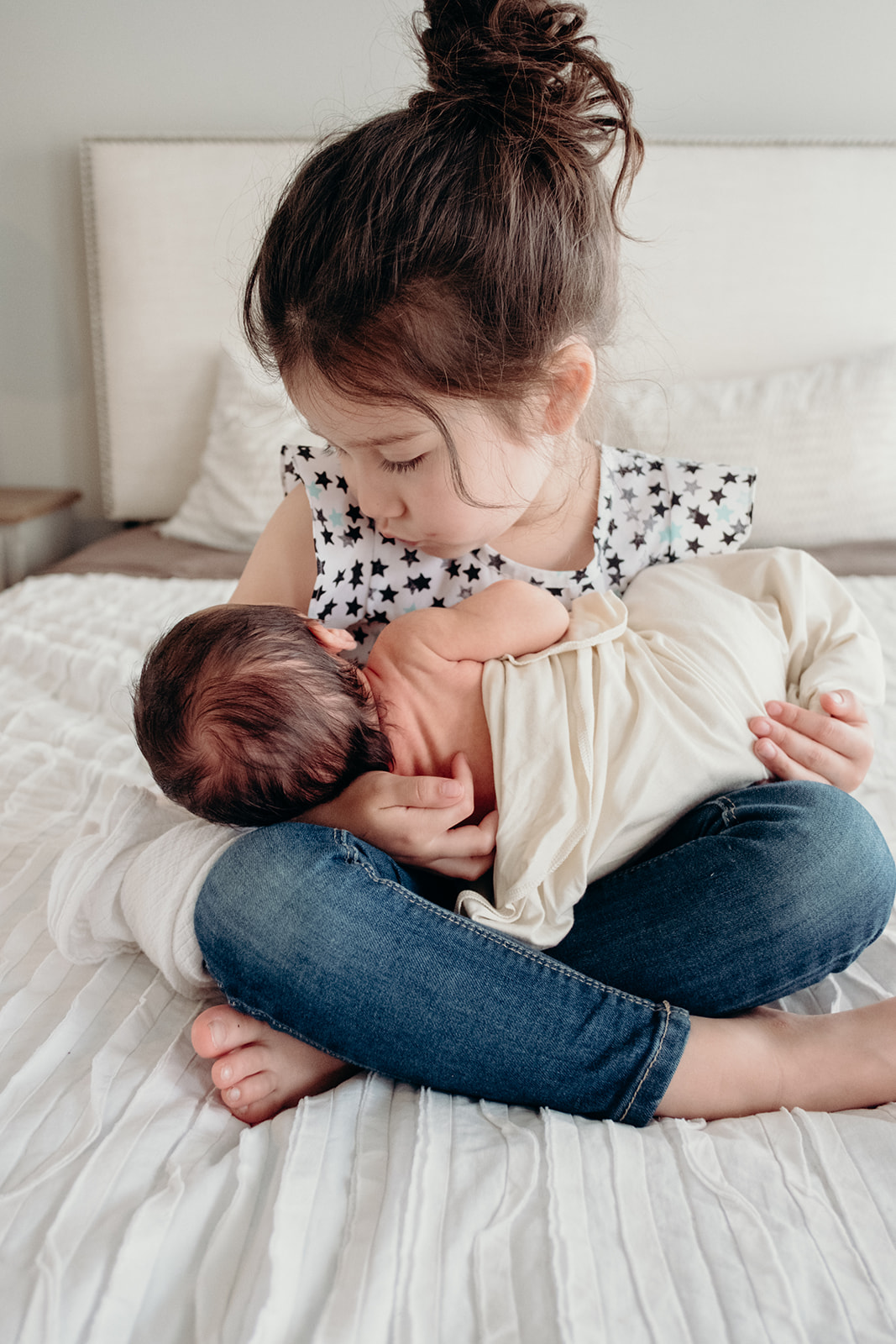 A little girl looks at her baby brother while holding him on her lap during an in home family photography session. 